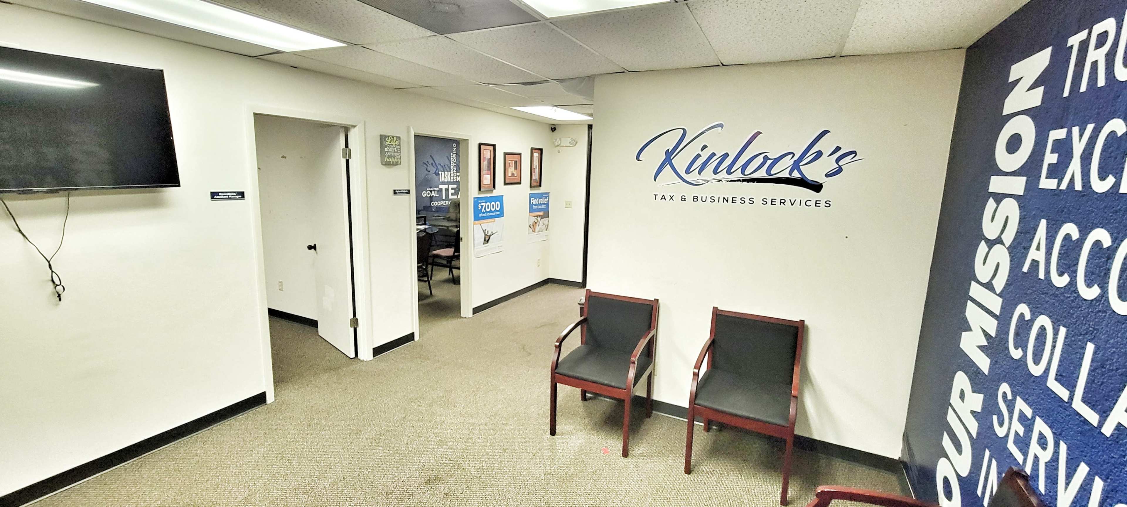 The image shows a small office interior with a waiting area featuring two chairs, a television on the left wall, and doorways leading to other rooms.