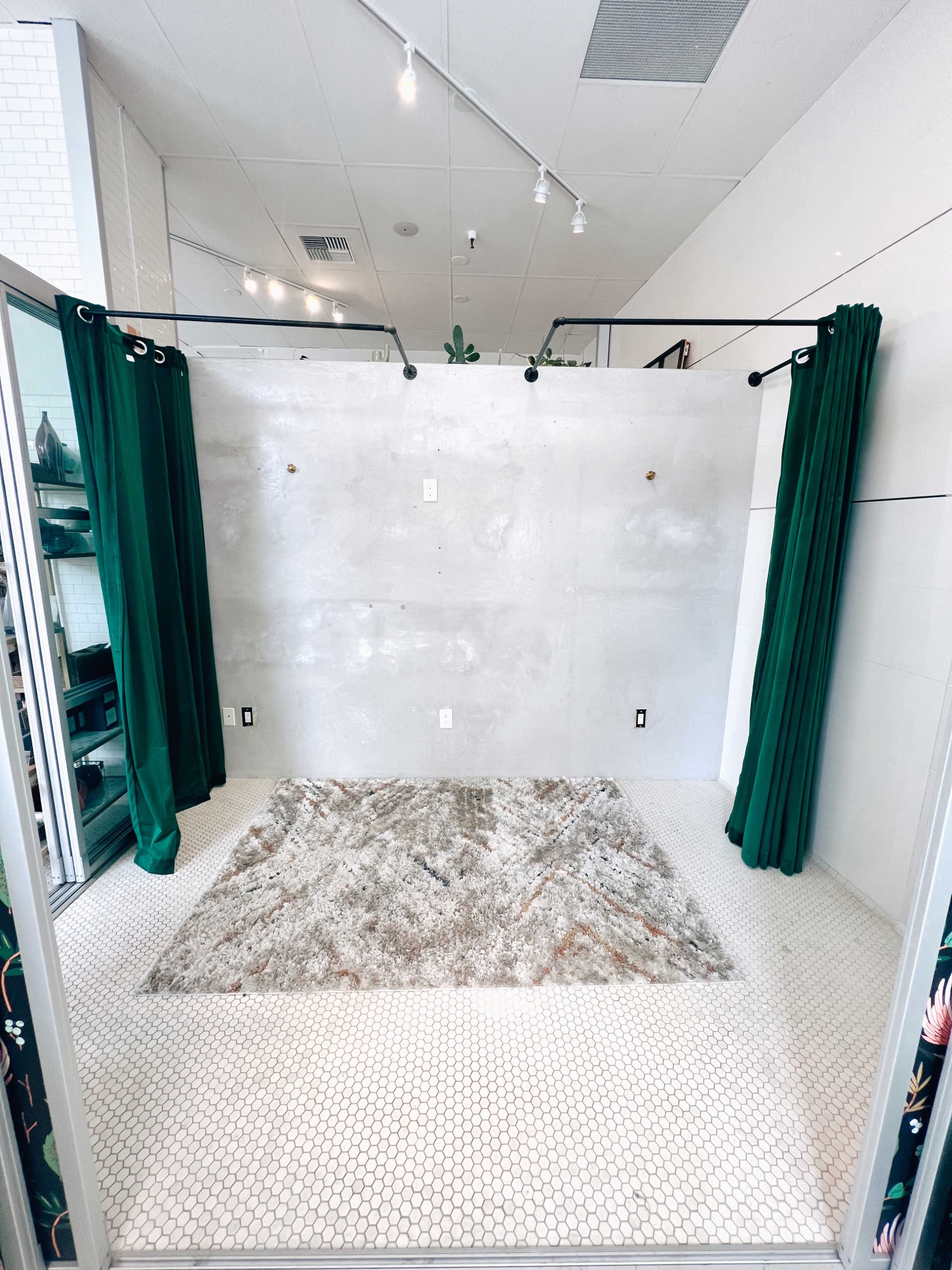 A minimalist room featuring a concrete wall, green curtains, and a patterned rug on a hexagonal tiled floor.