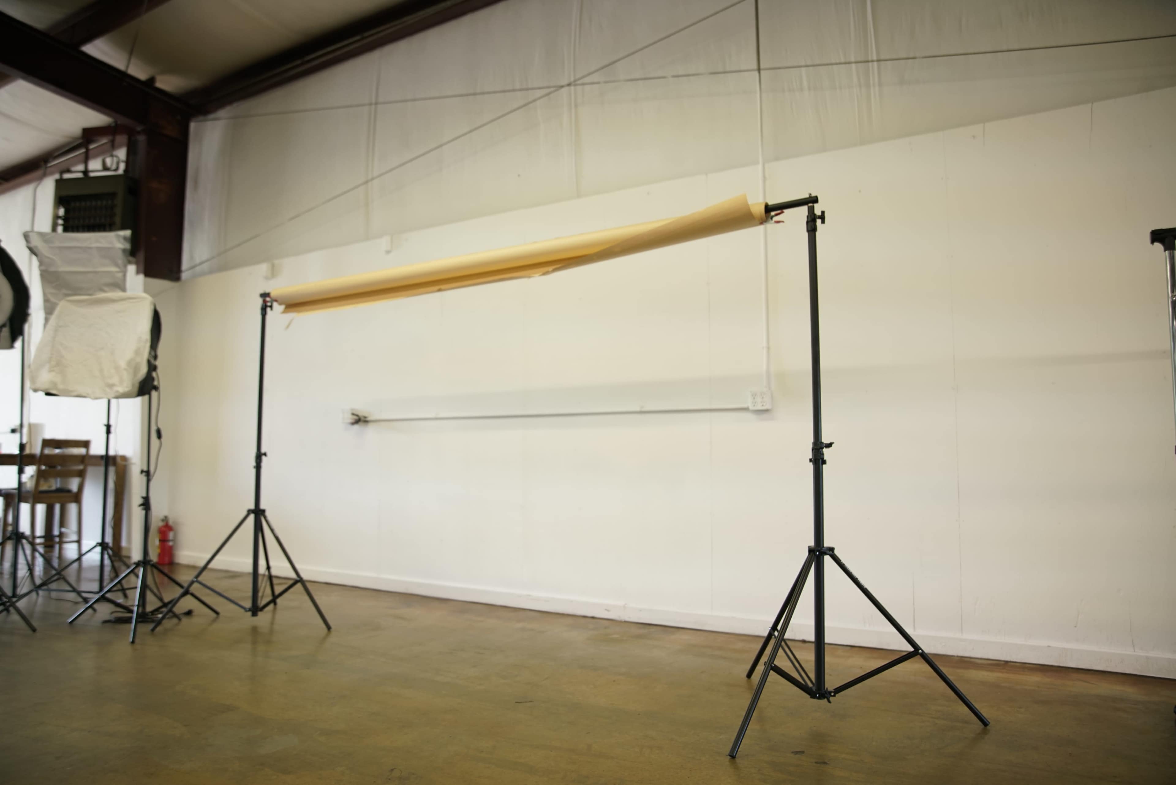 The image shows a photography setup with a backdrop roll supported by two sturdy stands in an empty studio space.
