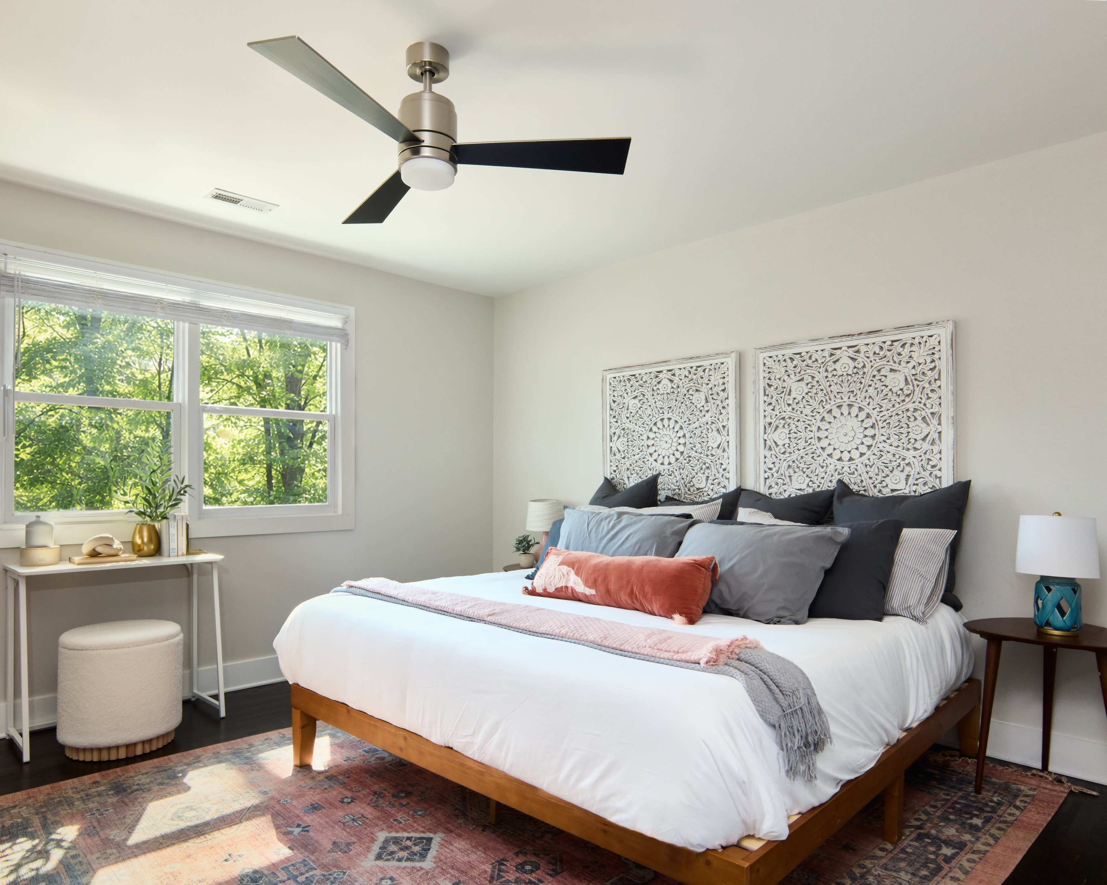 The image shows a neatly arranged bedroom with a large bed, decorative wall panels, and a window letting in natural light.