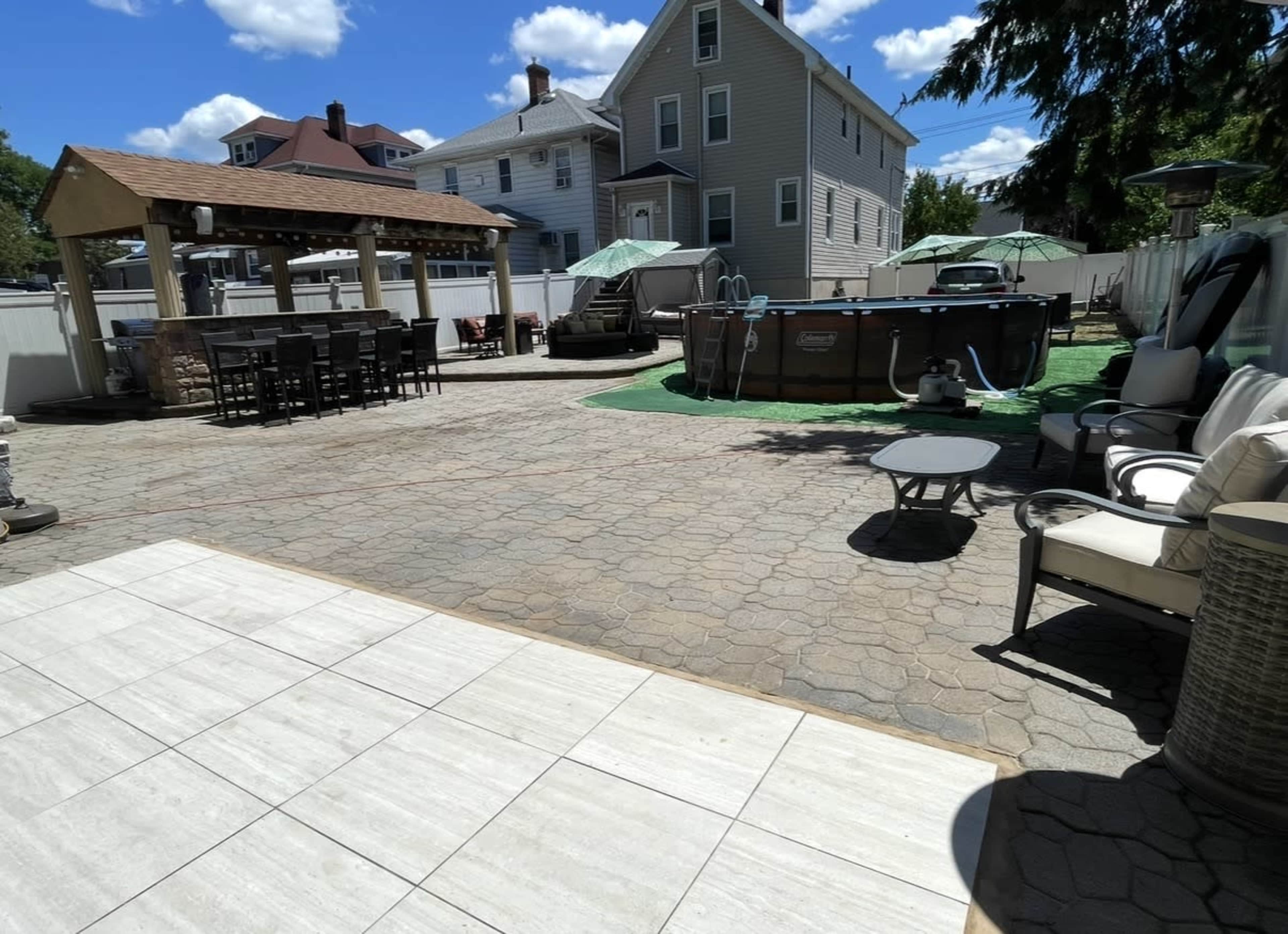 The image shows a backyard patio area featuring a swimming pool, outdoor seating, a gazebo structure, and a well-maintained lawn.