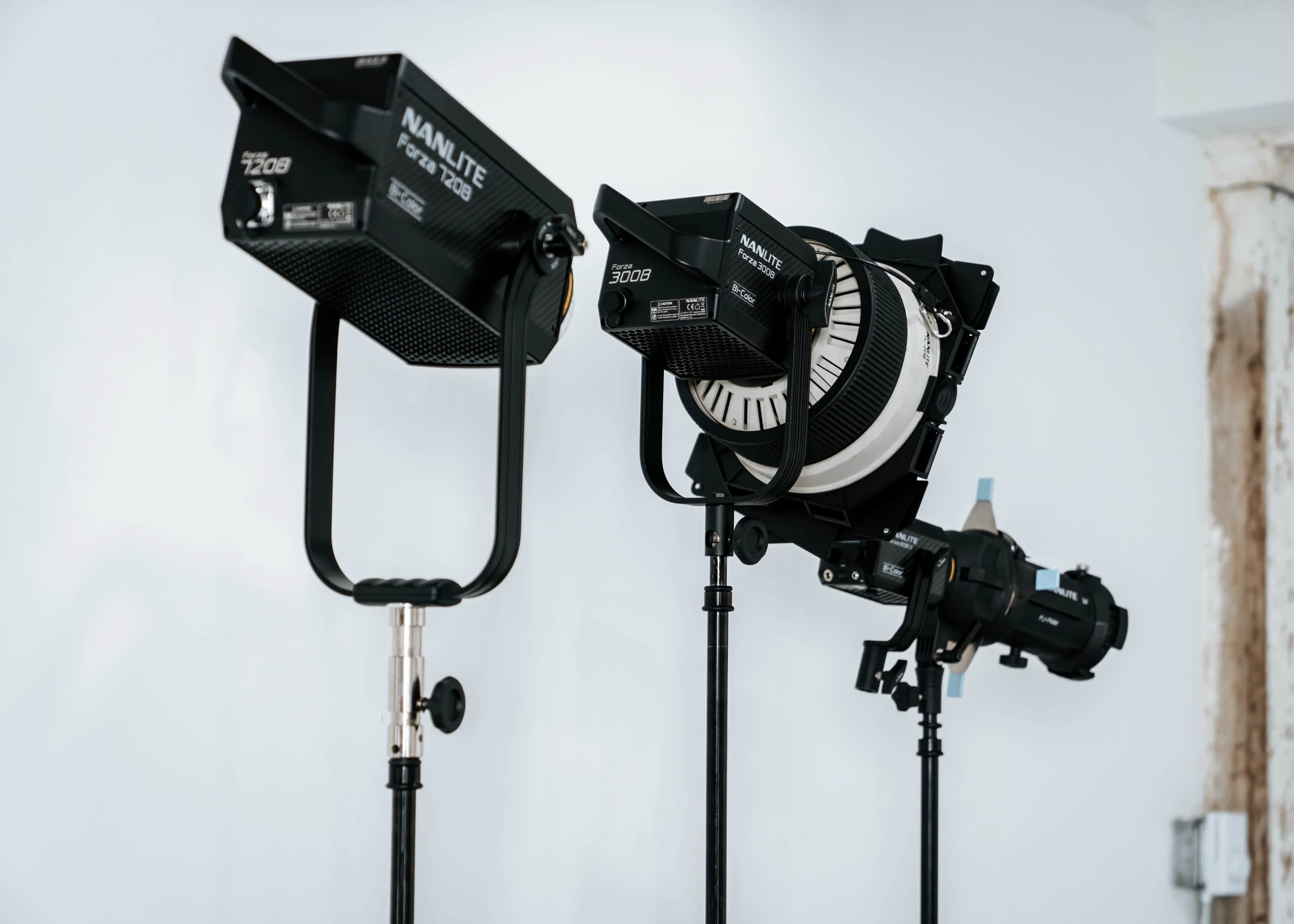 Two studio lights on stands are positioned against a white wall.