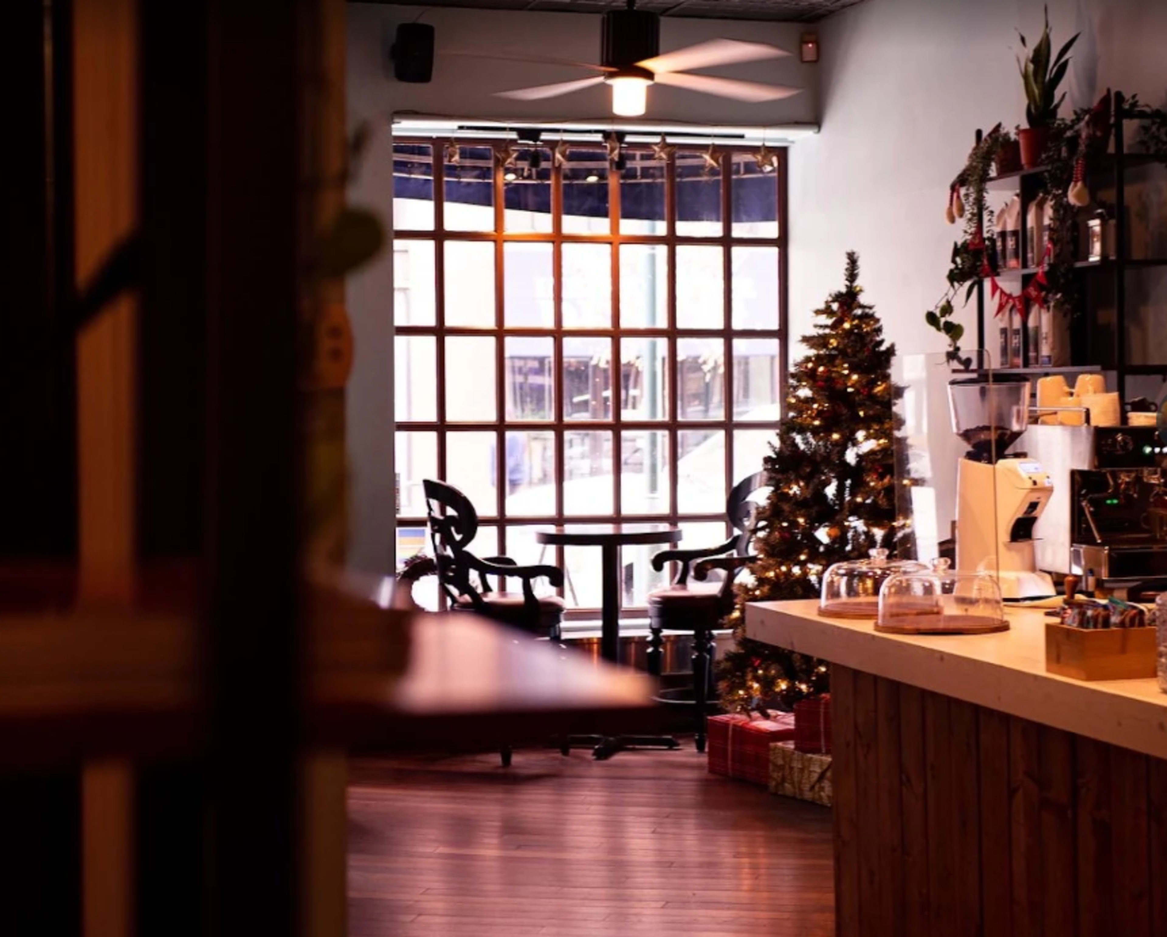 The image shows a cozy café interior with a decorated Christmas tree and a view of a window featuring a grid pattern.