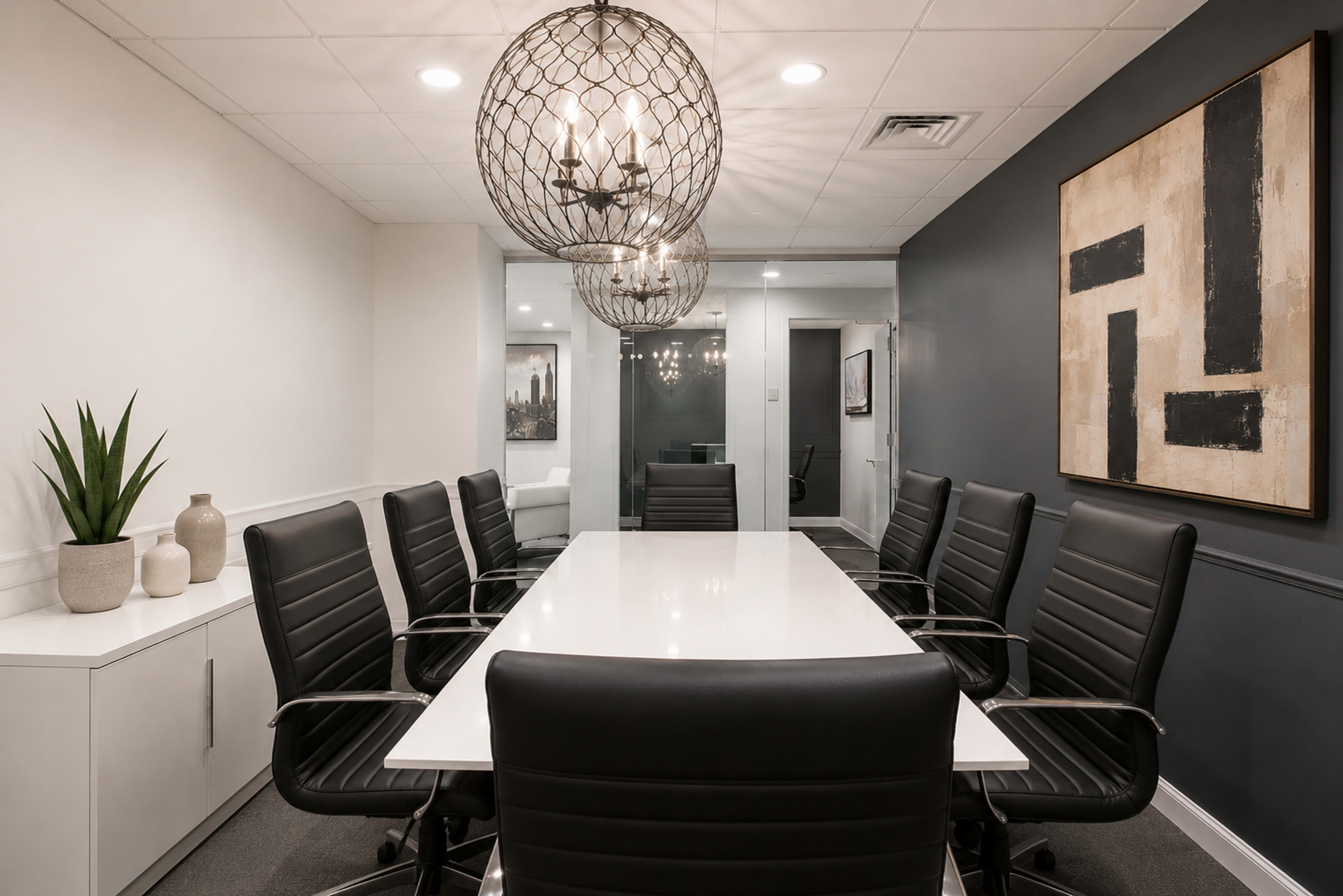 A modern conference room features a long white table surrounded by black leather chairs, illuminated by decorative hanging light fixtures.