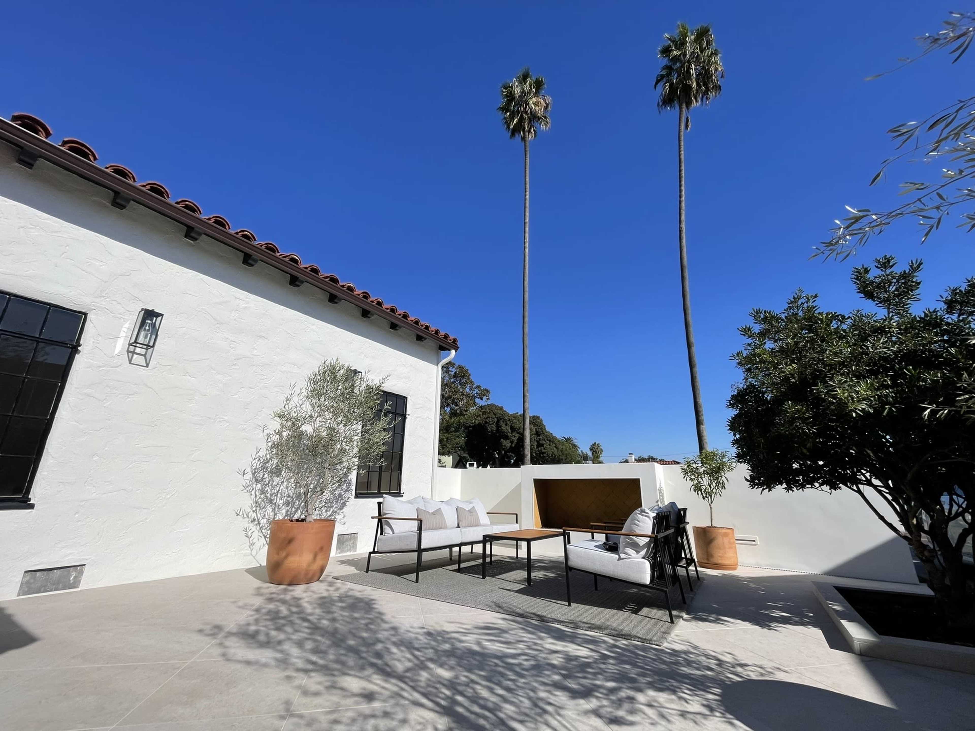 A patio area features a seating arrangement with a coffee table, surrounded by palm trees and a white stucco wall.
