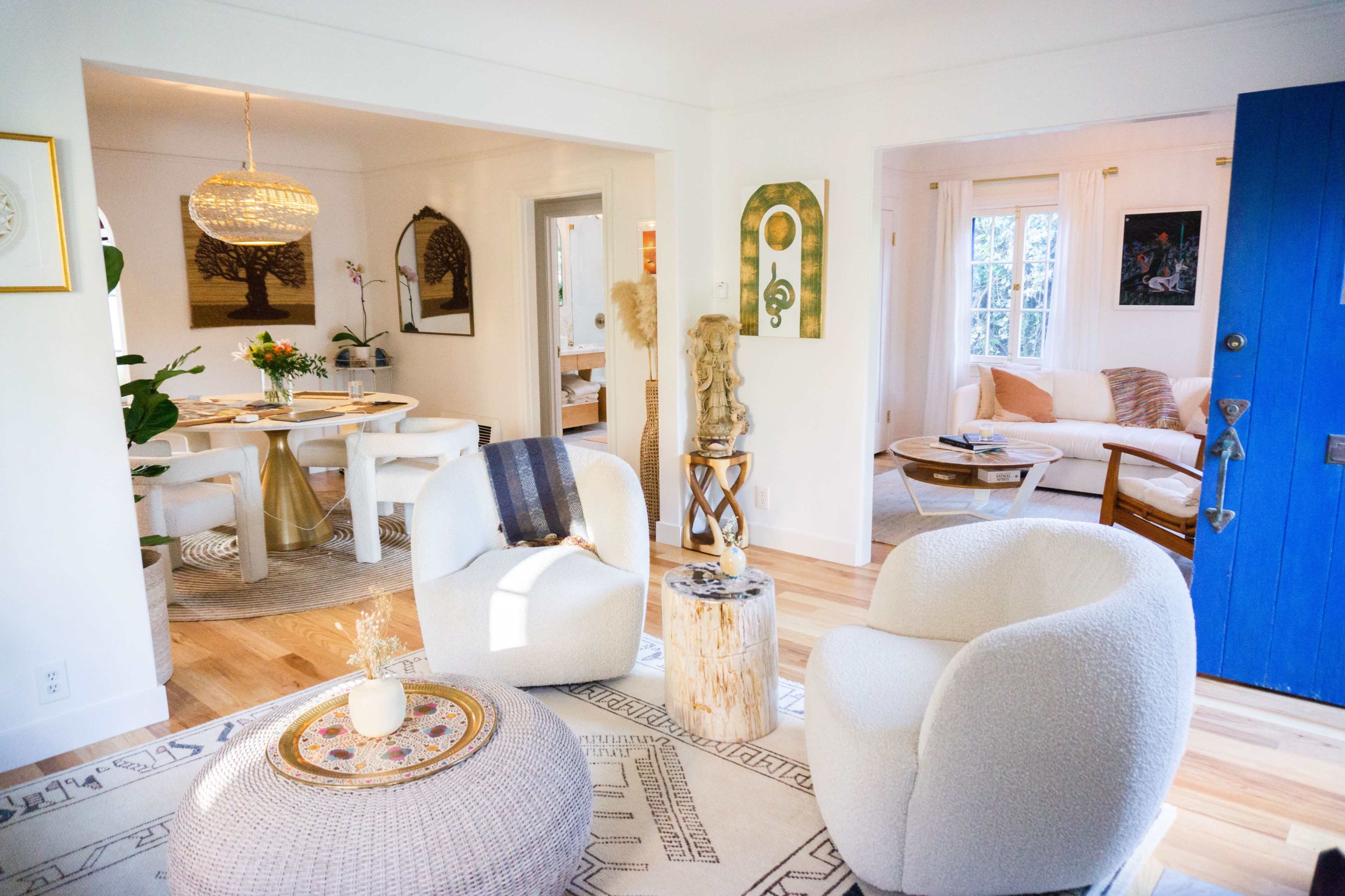 A bright, inviting living area featuring two cozy armchairs and a patterned rug, with an open view into a dining space adorned with a table and decorative plants.