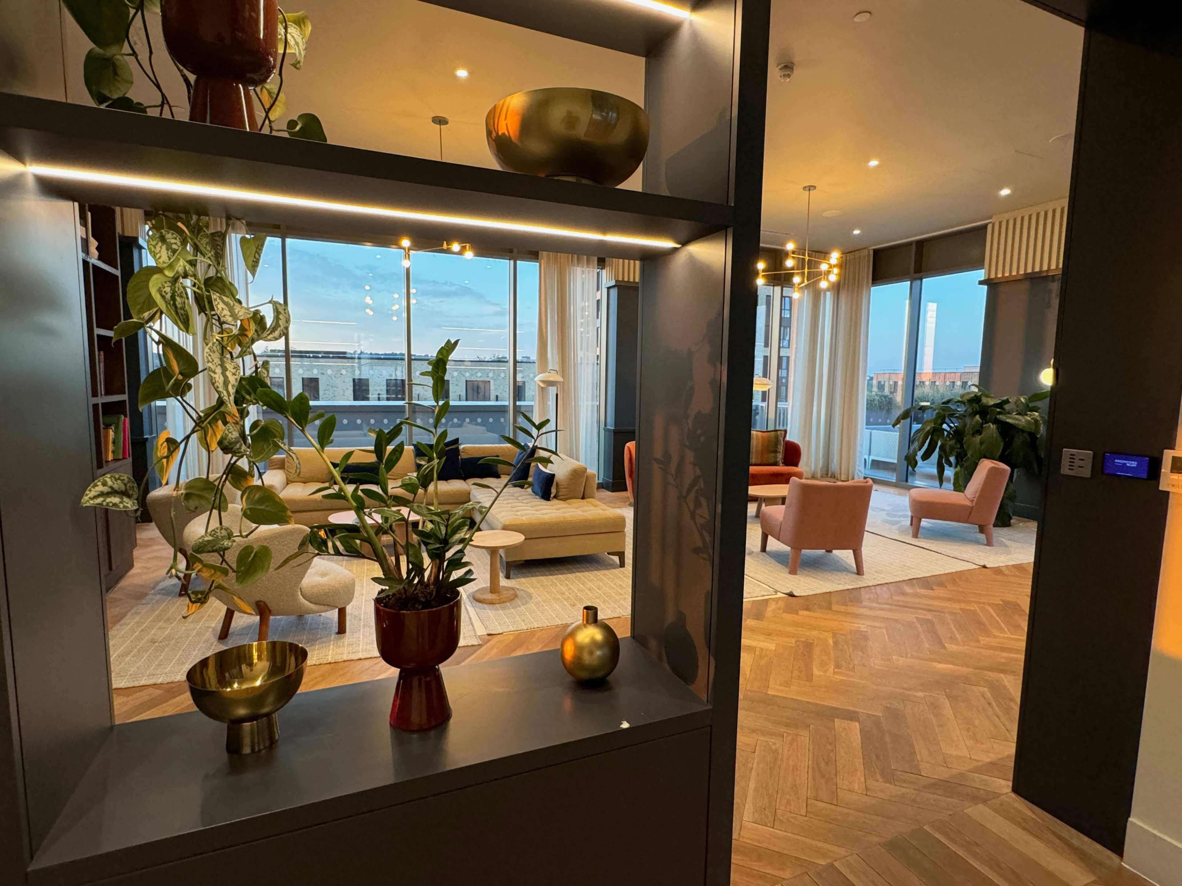 A modern interior living space with plants, decorative bowls, and various seating areas visible through a shelf.