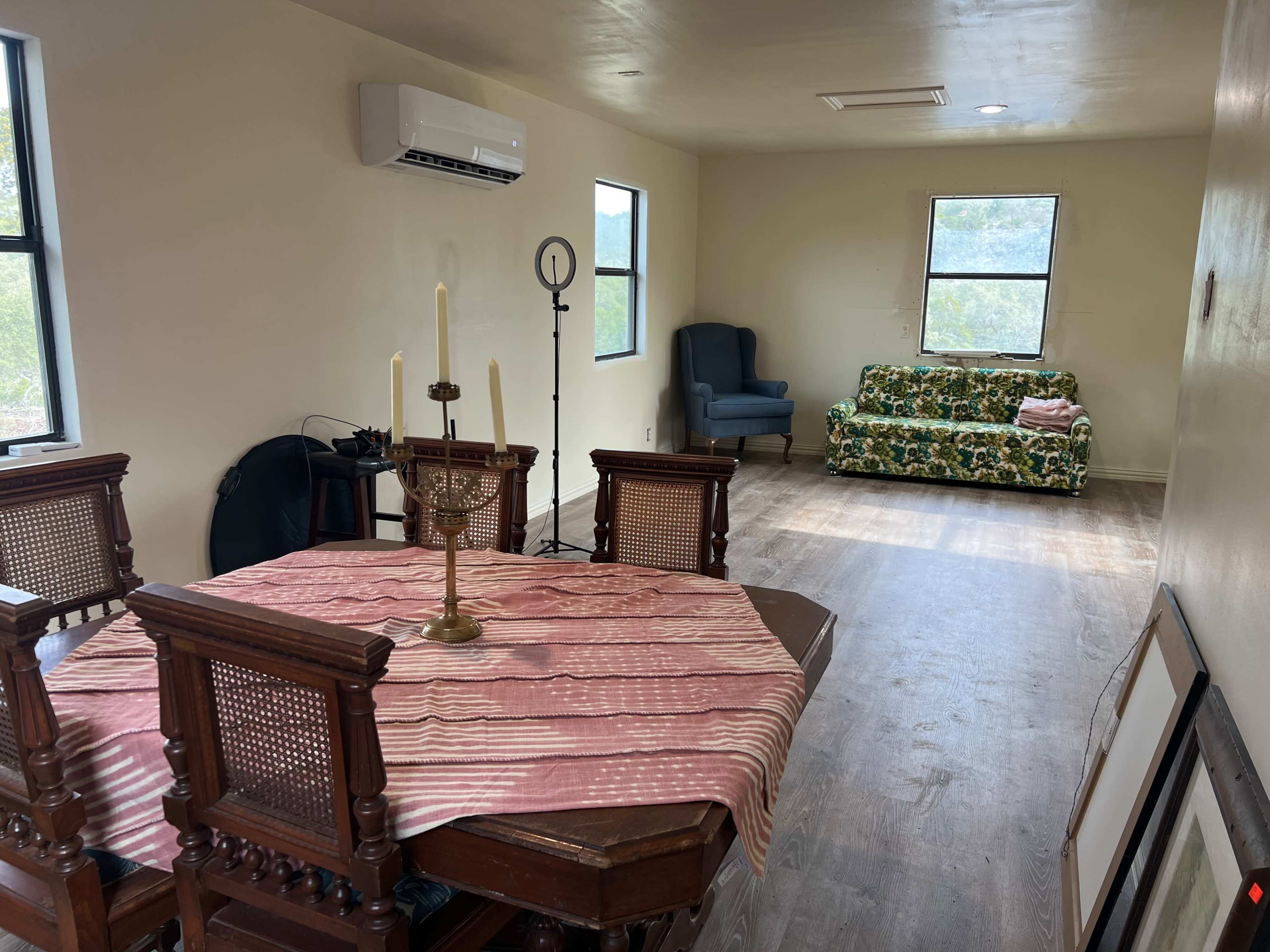 The image shows a room featuring a dining table with four chairs, a green floral couch, and two windows letting in natural light.