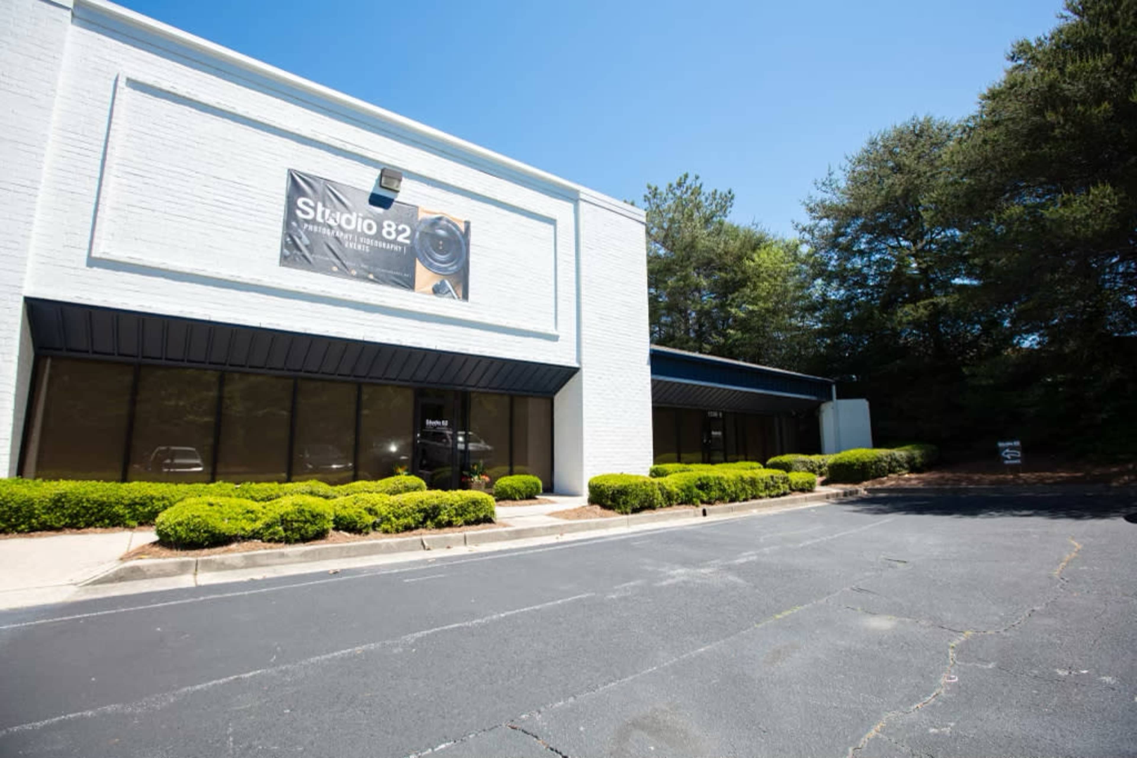 The image shows a white commercial building named "Studio 82," flanked by neatly trimmed bushes and surrounded by a clear blue sky.