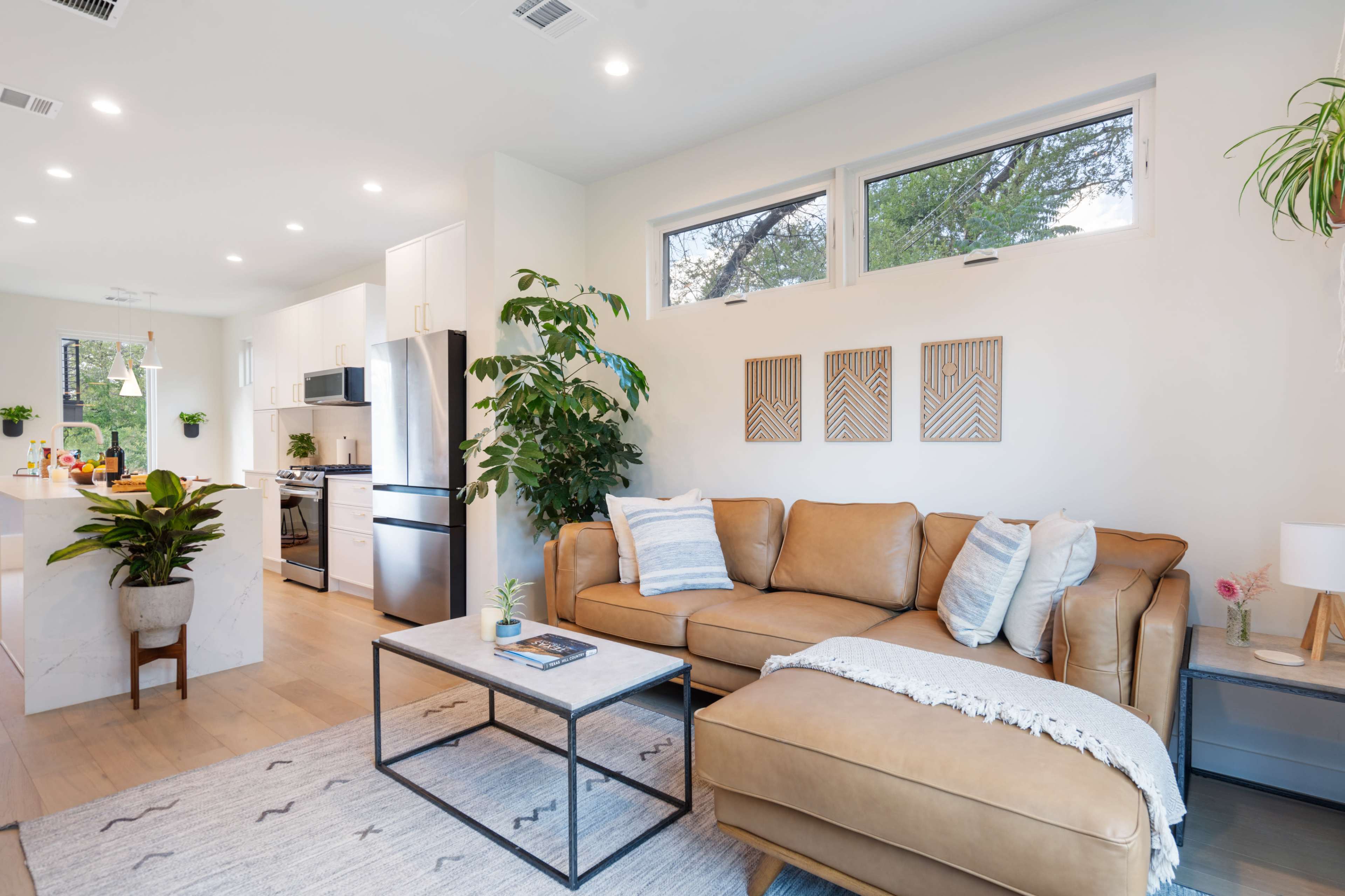 The image depicts a modern living room with a tan leather sectional sofa, a coffee table, and large windows allowing natural light to illuminate the space.