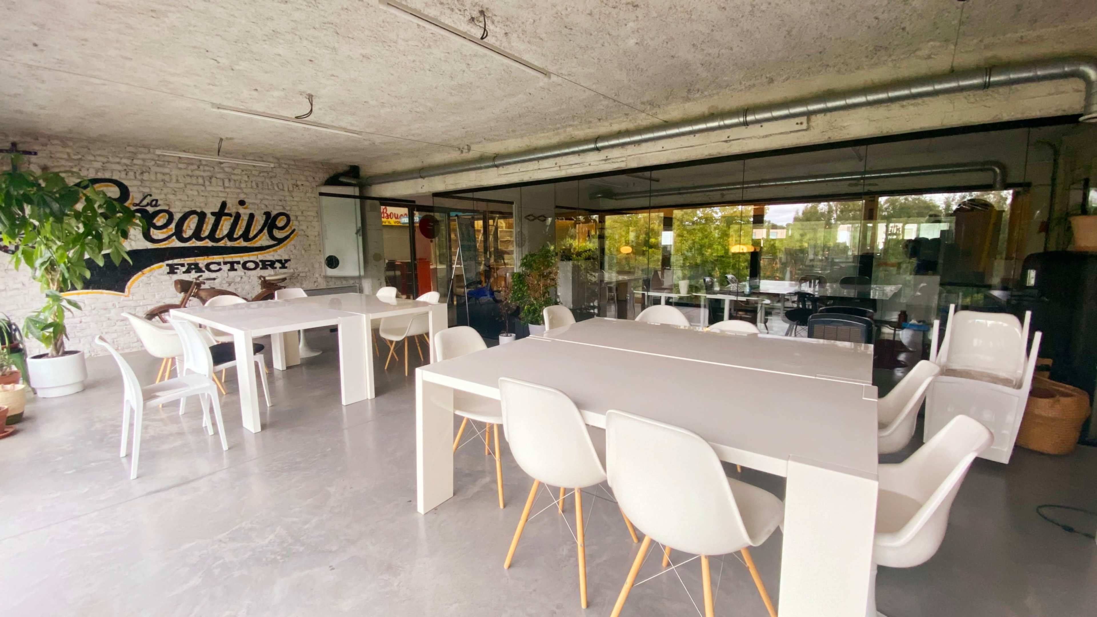 The image shows a modern interior space with white tables and chairs, large windows, and greenery, labeled as "Creative Factory."