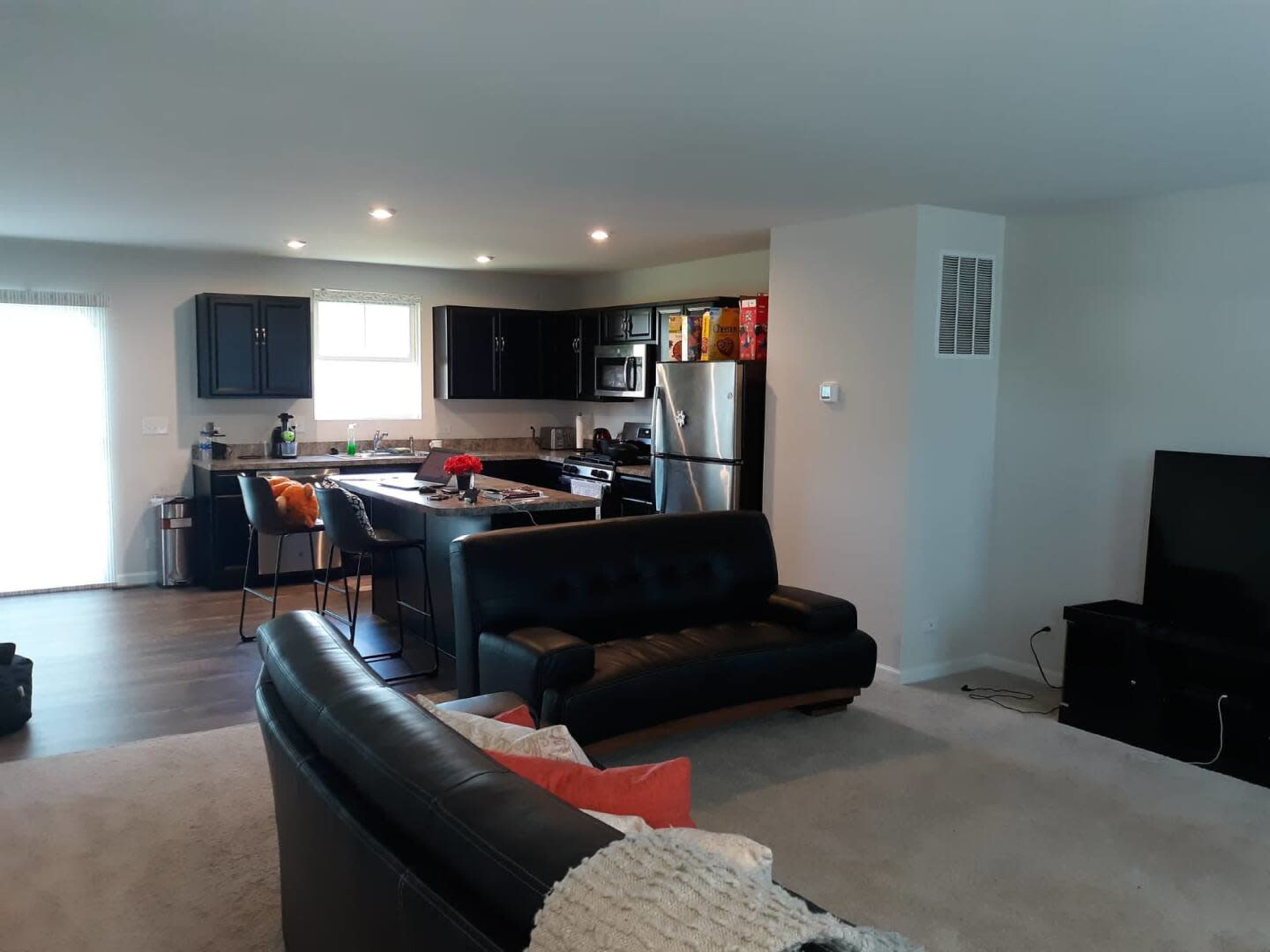 A modern open-concept living room and kitchen area with black cabinets, stainless steel appliances, and a black leather sofa.