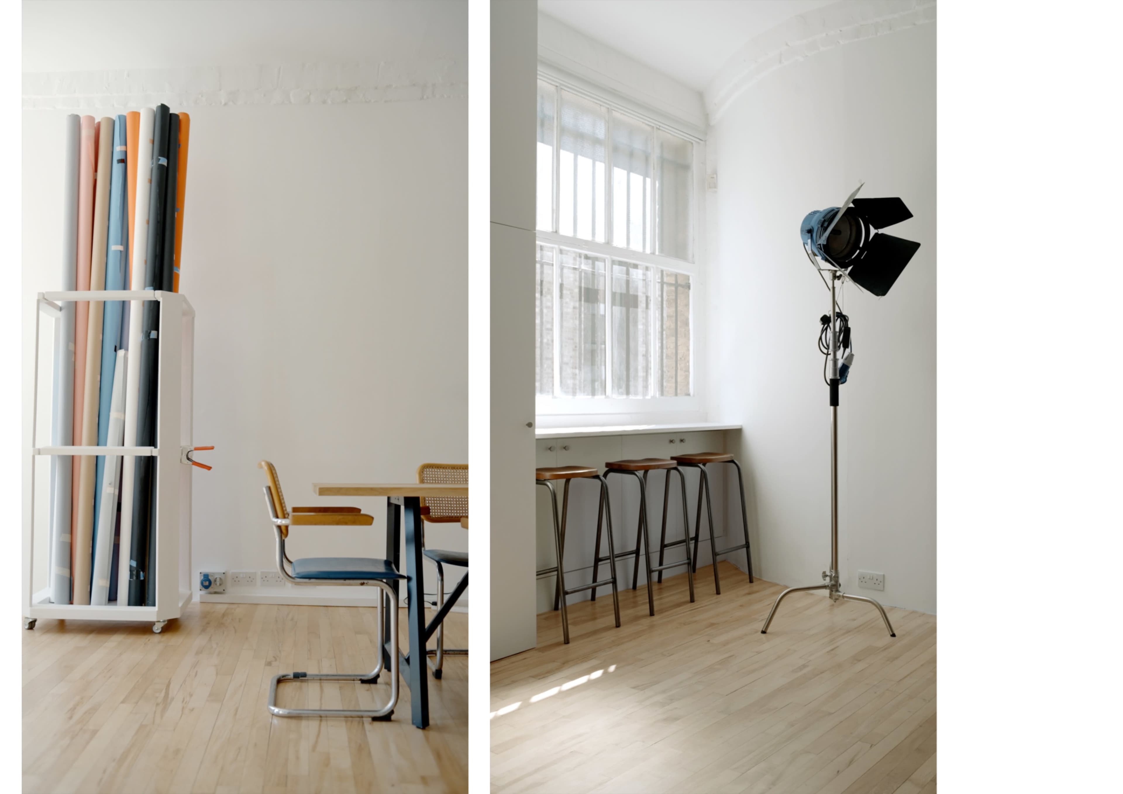 A minimalist studio space with a rack of colorful backdrops on one side and a lighting setup next to a table and stools on the other.