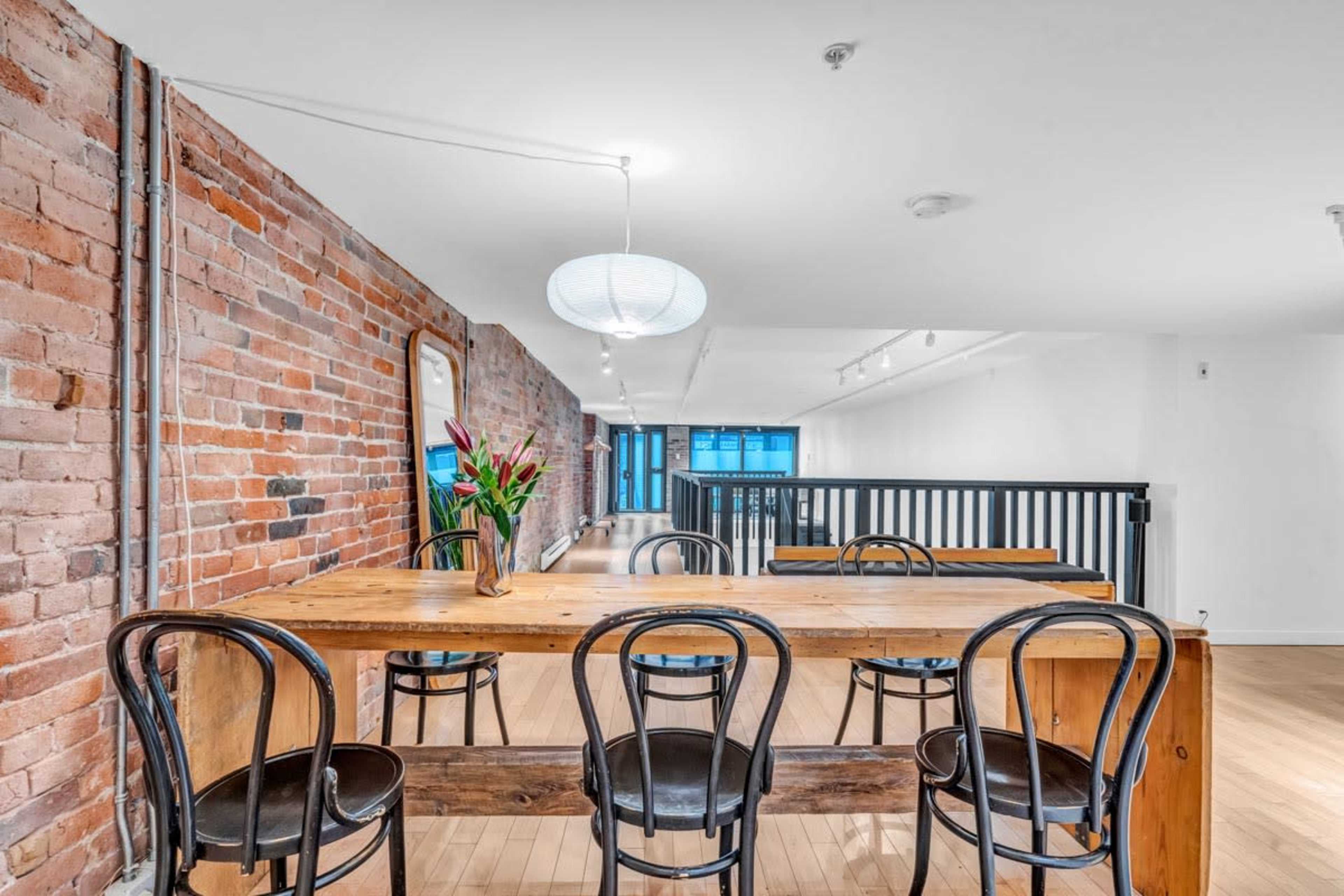 A dining area with a wooden table and black chairs, set against a backdrop of exposed brick walls and minimalistic lighting.