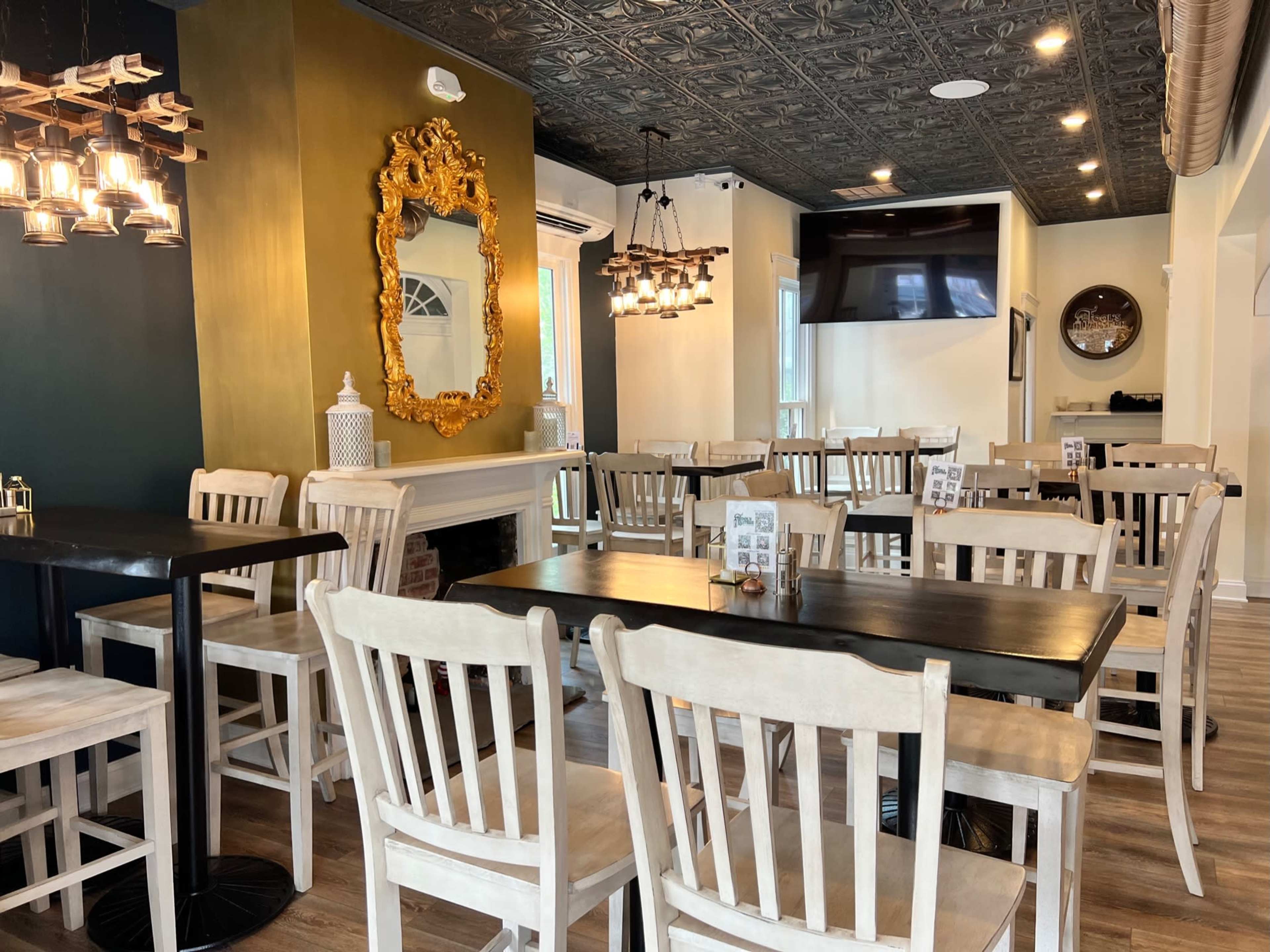 A restaurant interior with wooden tables and chairs, decorative mirrors, and a mix of pendant and wall lighting.
