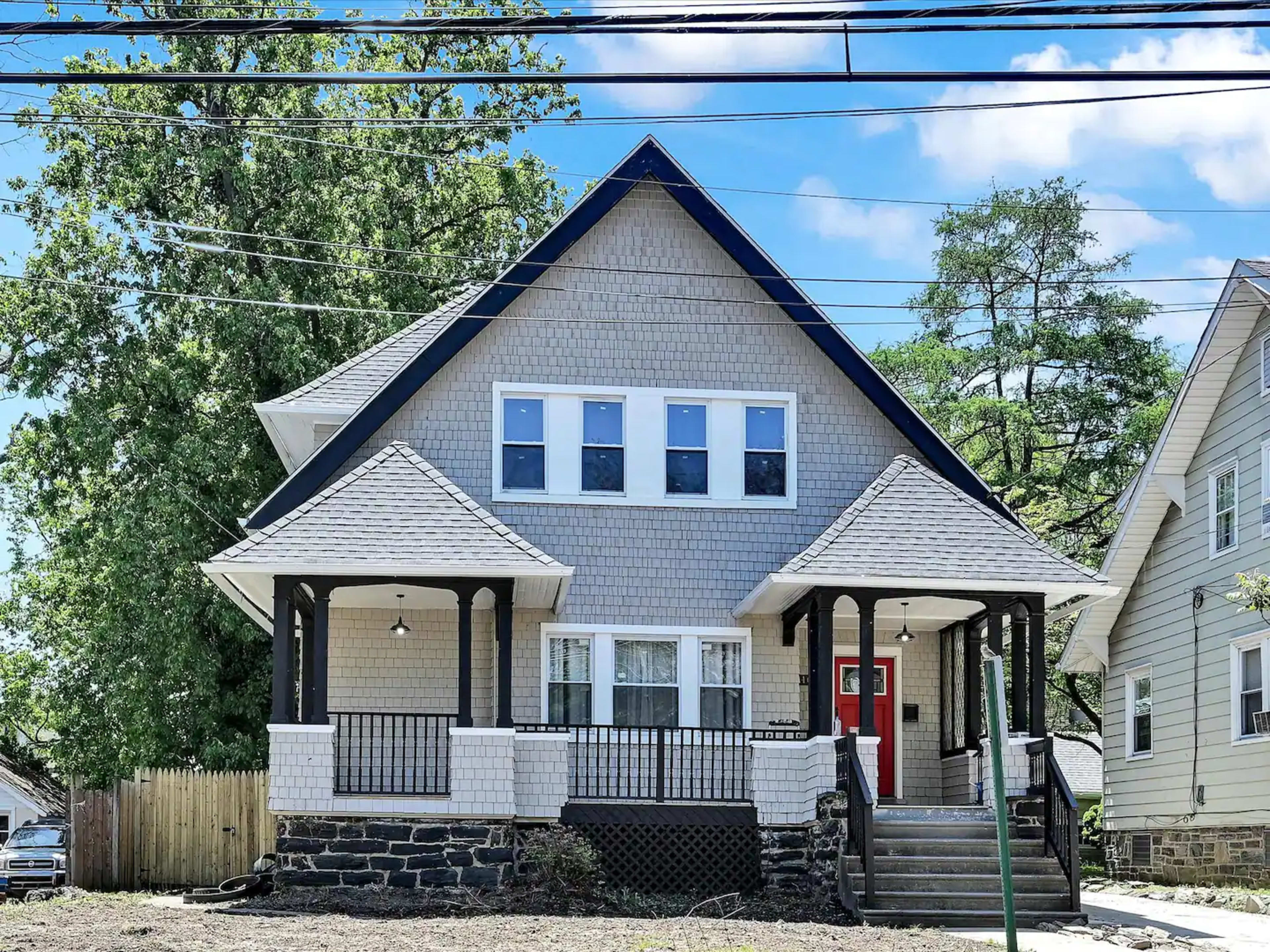 The image shows a large, two-story house with a gabled roof, front porch, and multiple windows, located in a residential area.
