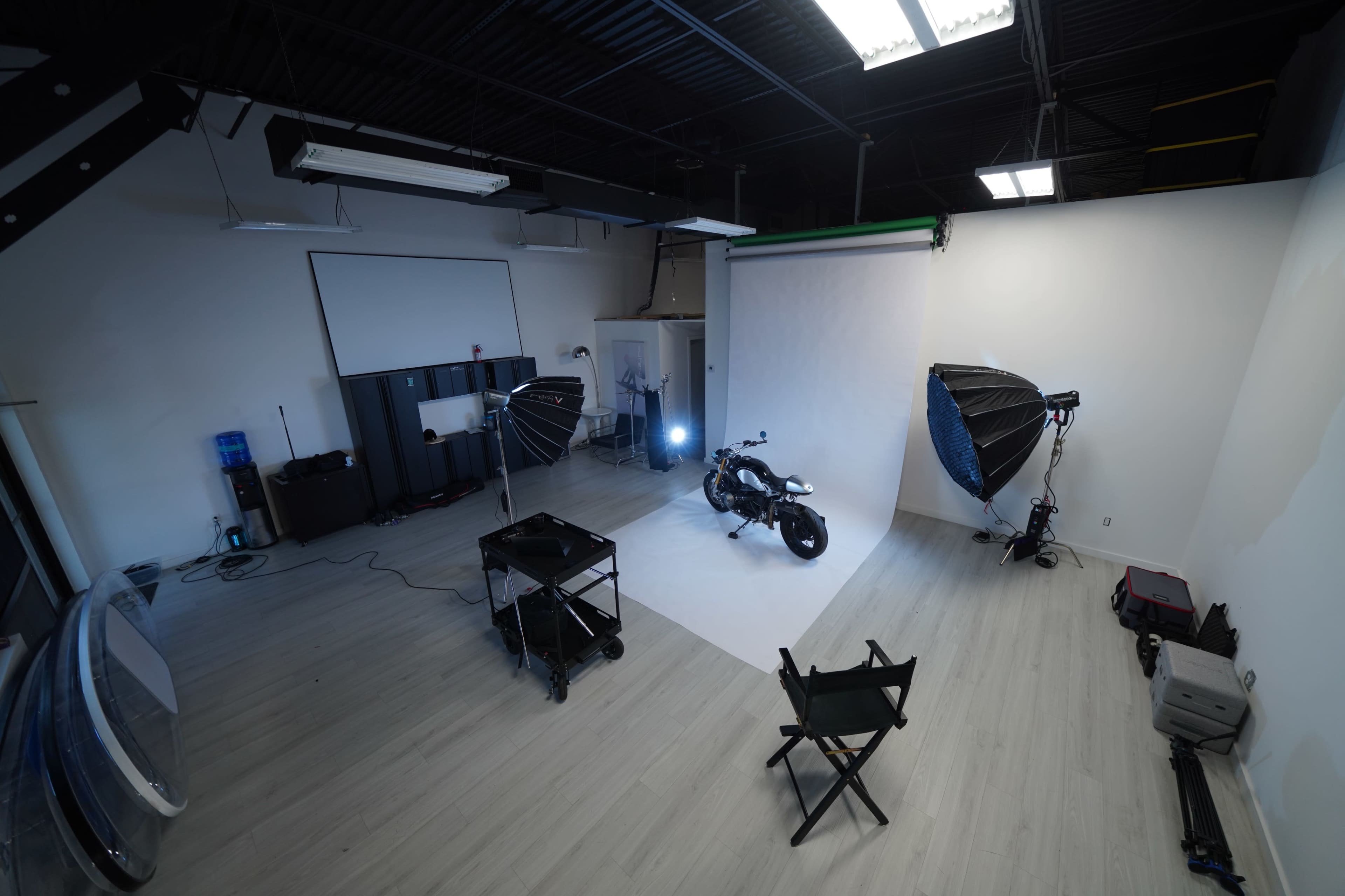 A spacious photography studio features a motorcycle positioned on a white backdrop, illuminated by multiple softbox lights.