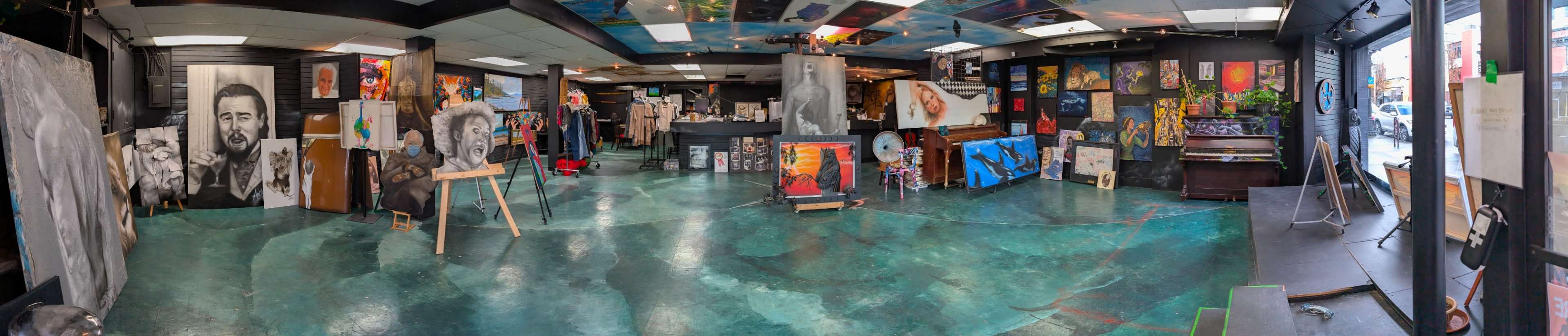 The image shows an art gallery featuring a variety of paintings and artworks displayed on the walls and easels, with a polished concrete floor and a reception area in the background.