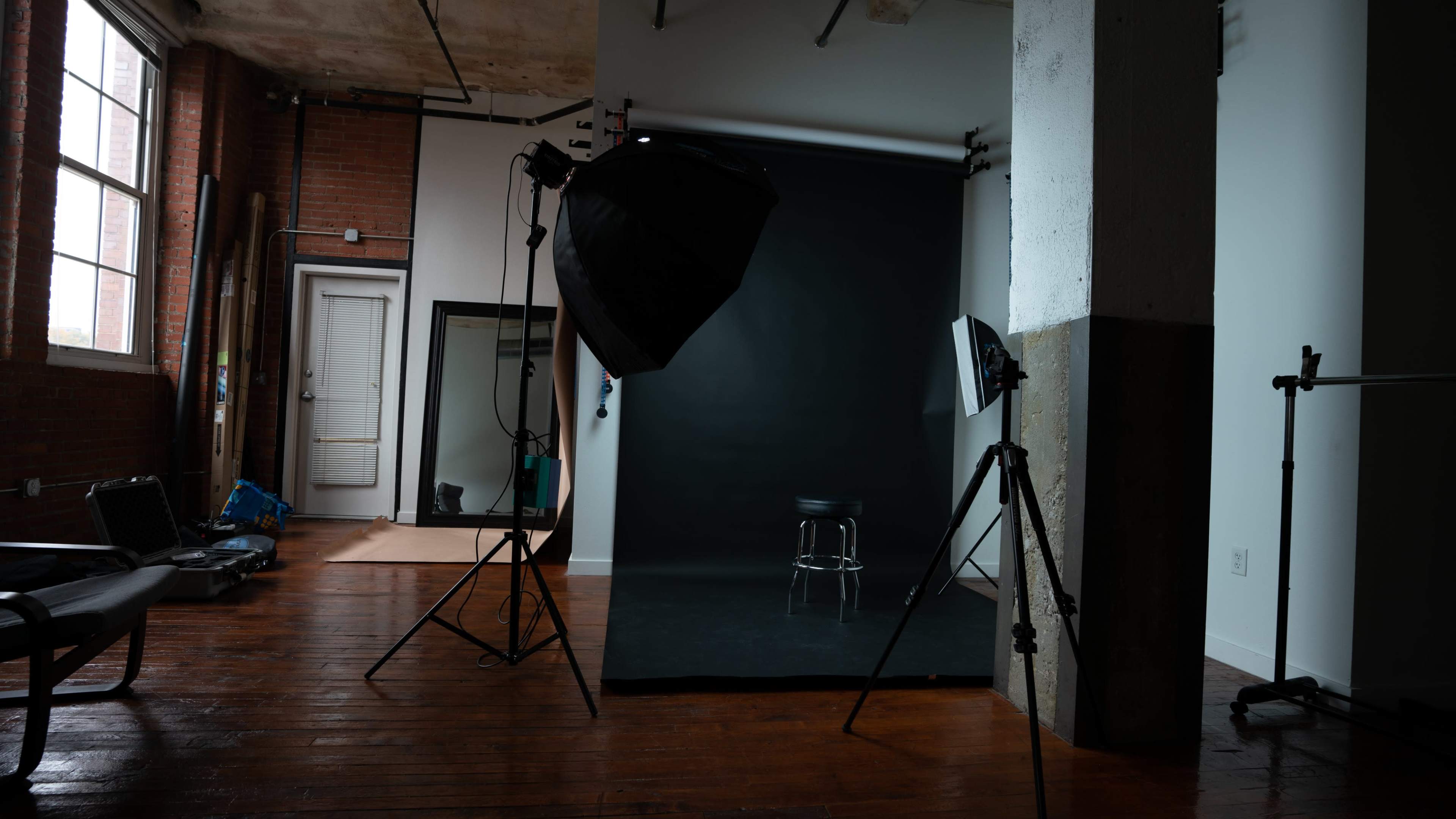 A photography studio with a black backdrop, a stool, and lighting equipment positioned on wooden floors.