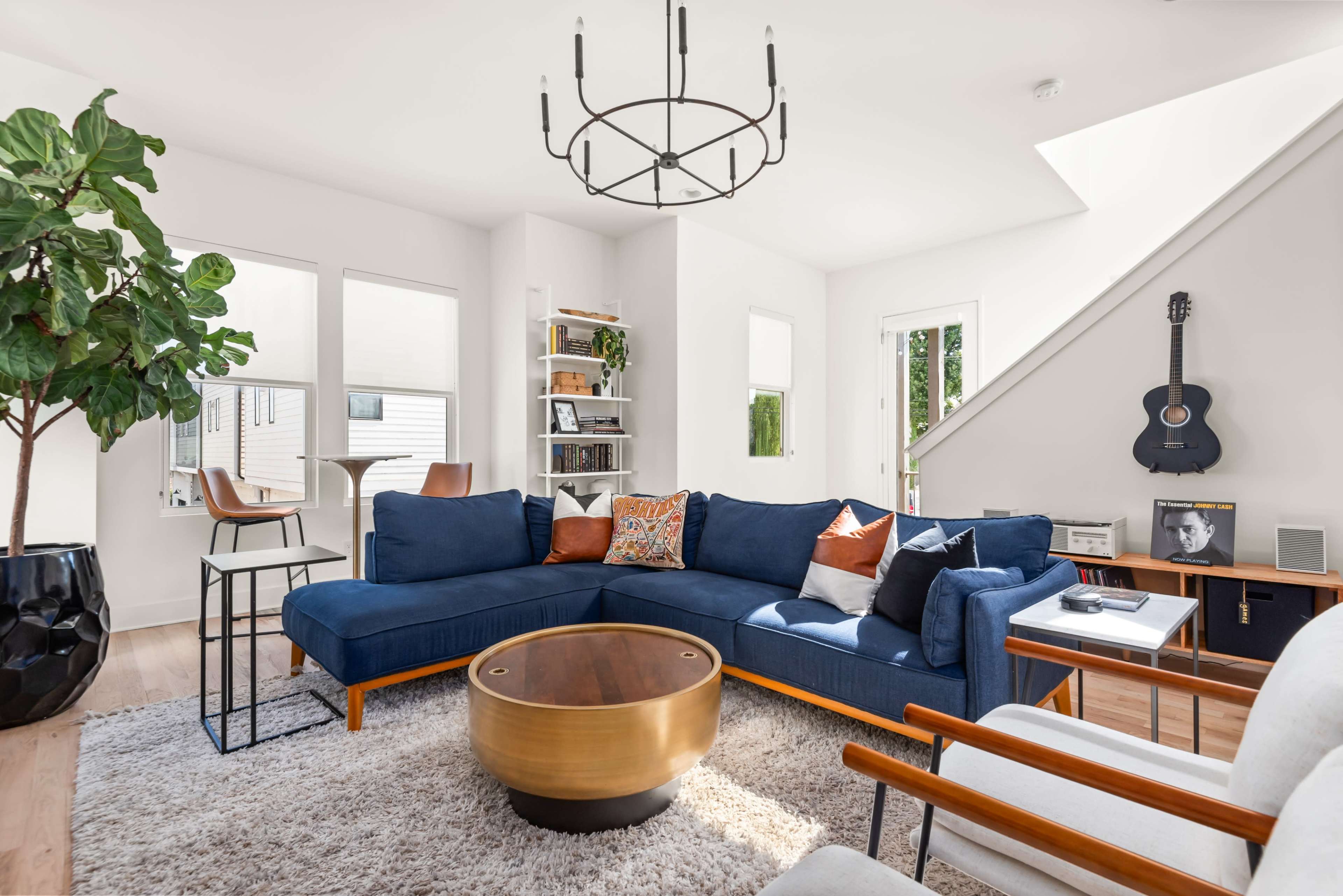 A modern living room features a blue sectional sofa, a round coffee table, and a guitar on the wall, accented by large windows and a skylight.