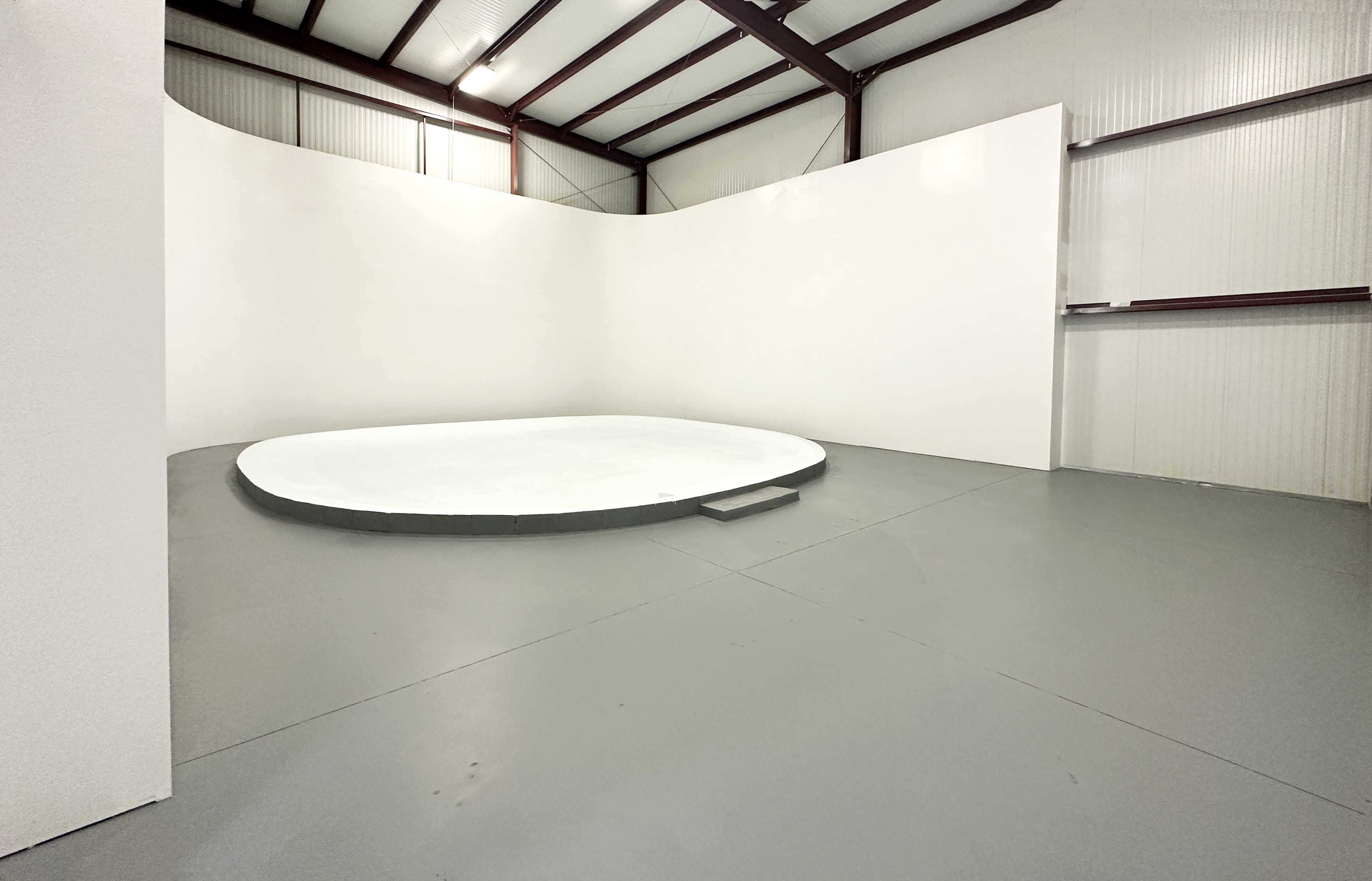 The image shows an empty, circular platform in a spacious, well-lit industrial building with white walls and a concrete floor.