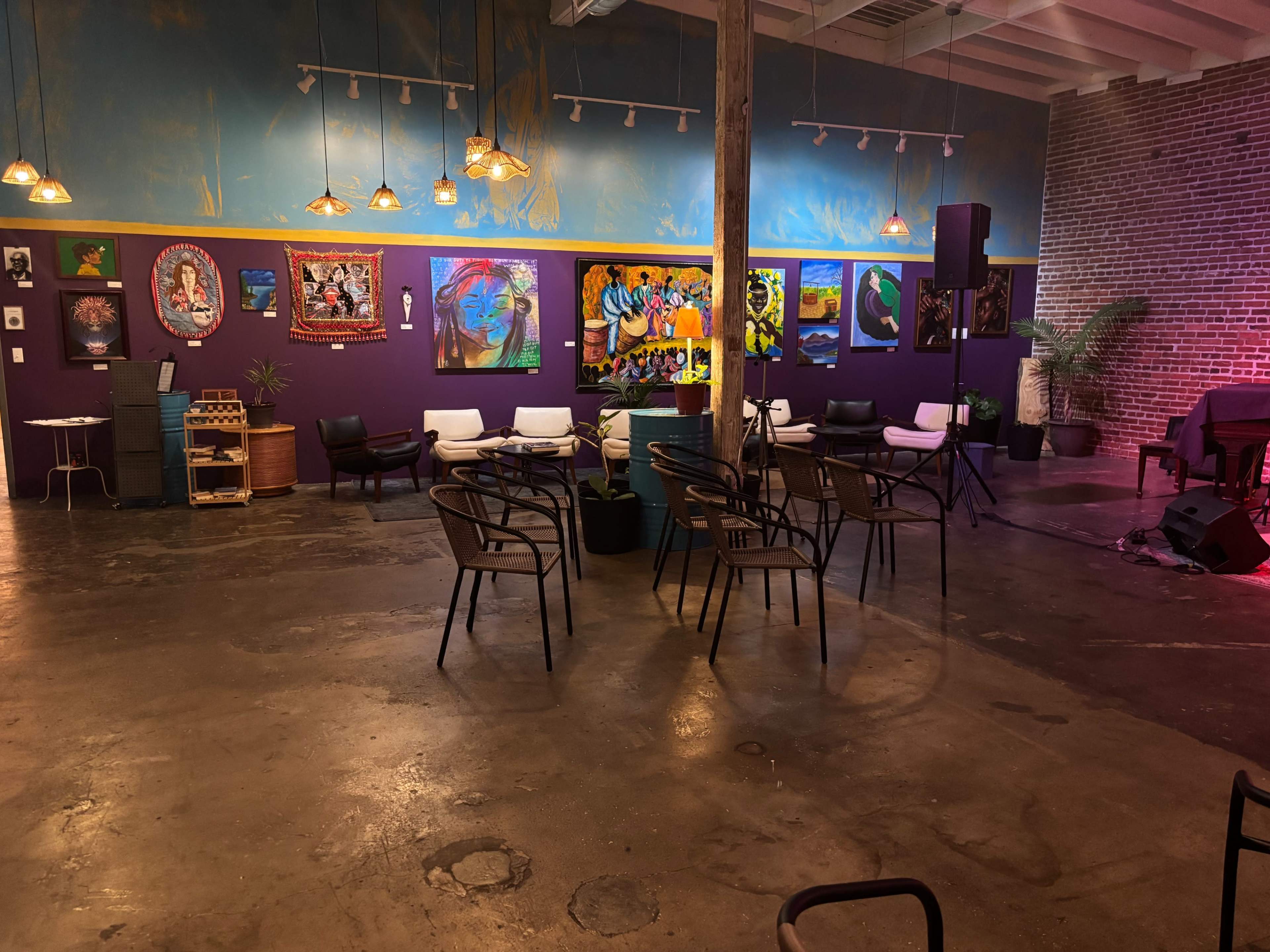 The image shows an artistic interior space with colorful wall art, seating arrangements, and a small stage area for live performances.