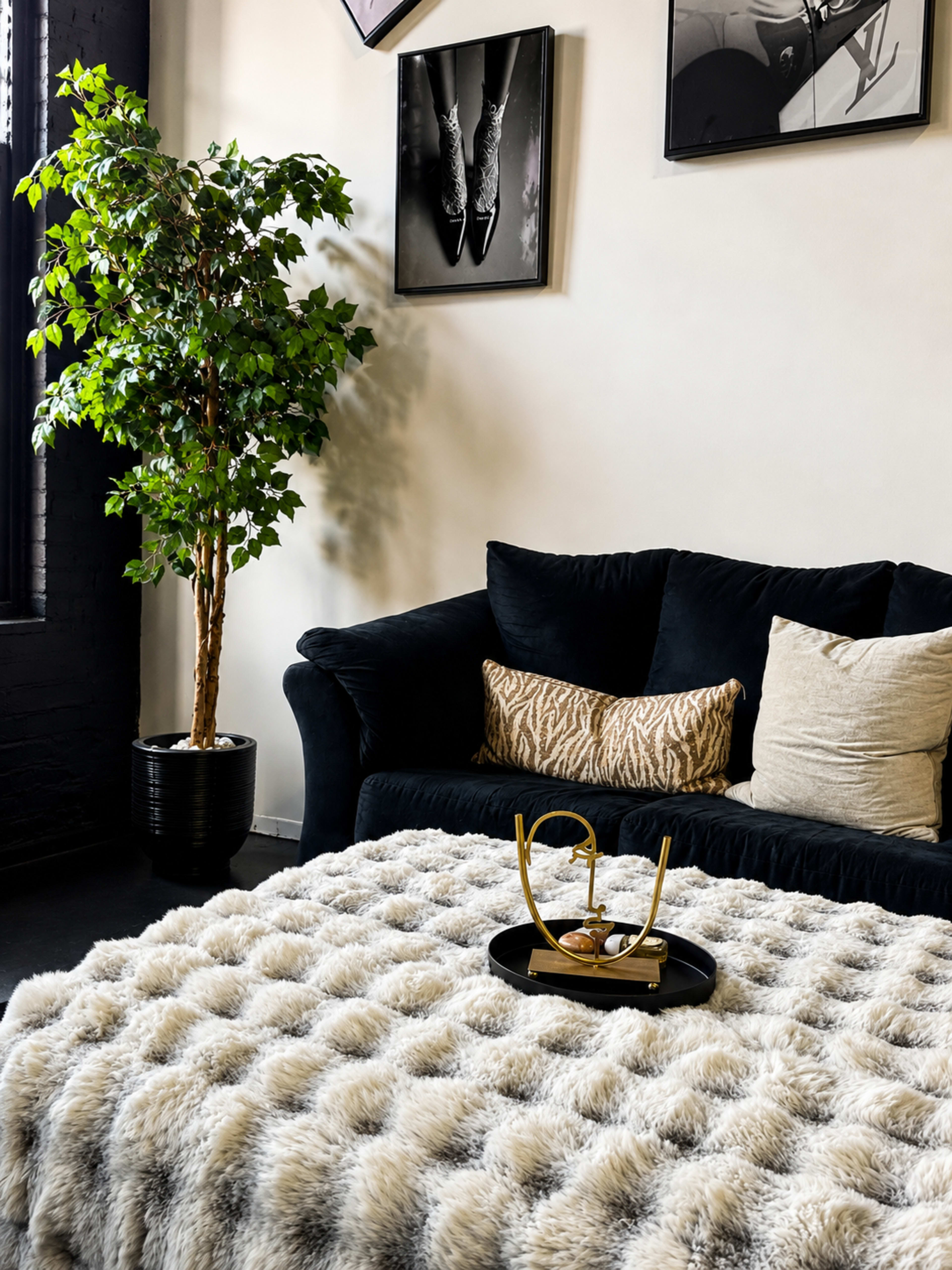 The image features a dark-colored sofa adorned with cushions, a fluffy textured throw blanket on a table in front, and a decorative plant in a pot nearby.