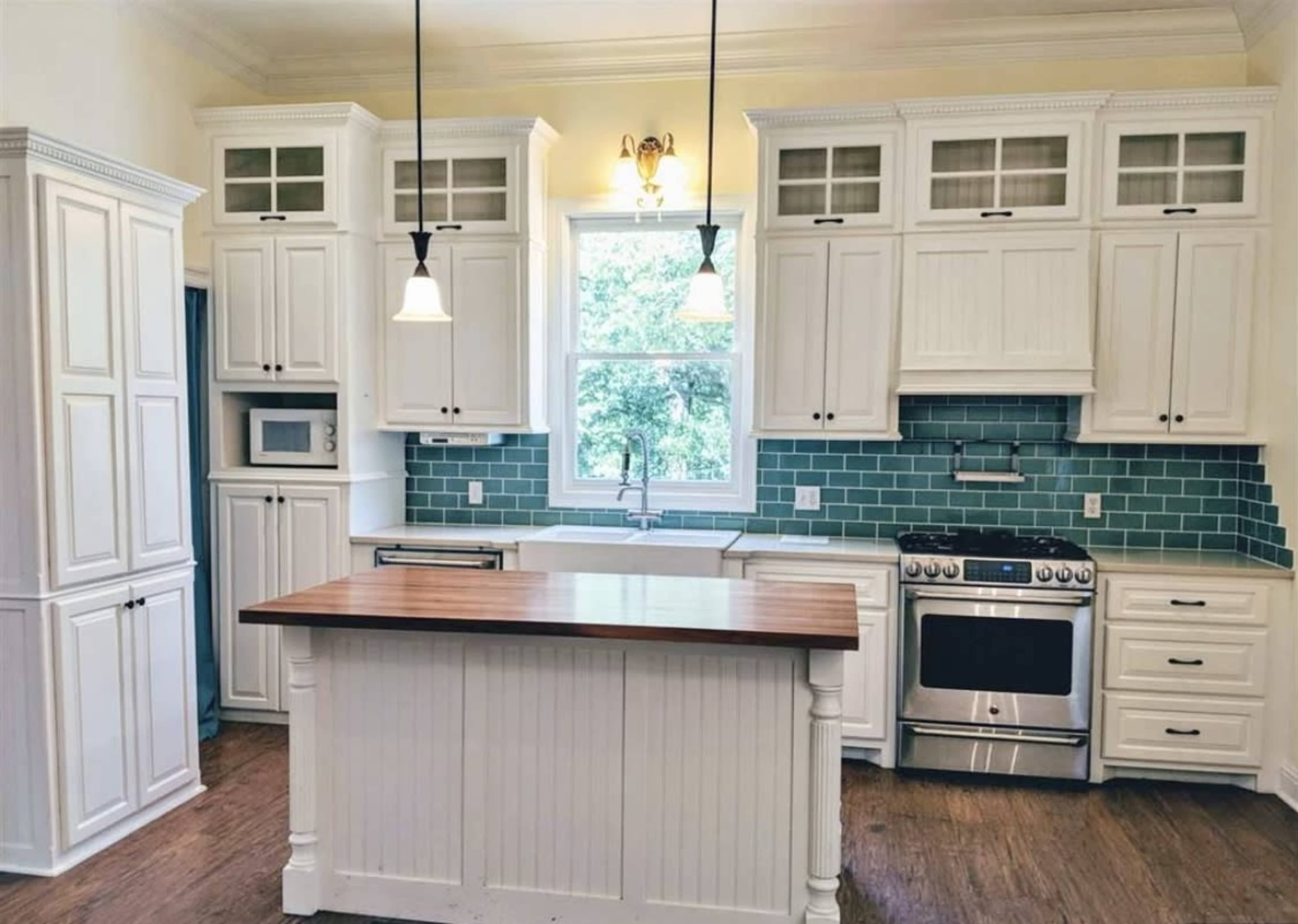 A modern kitchen features white cabinetry, a central wooden island, and a tiled backsplash in shades of blue.