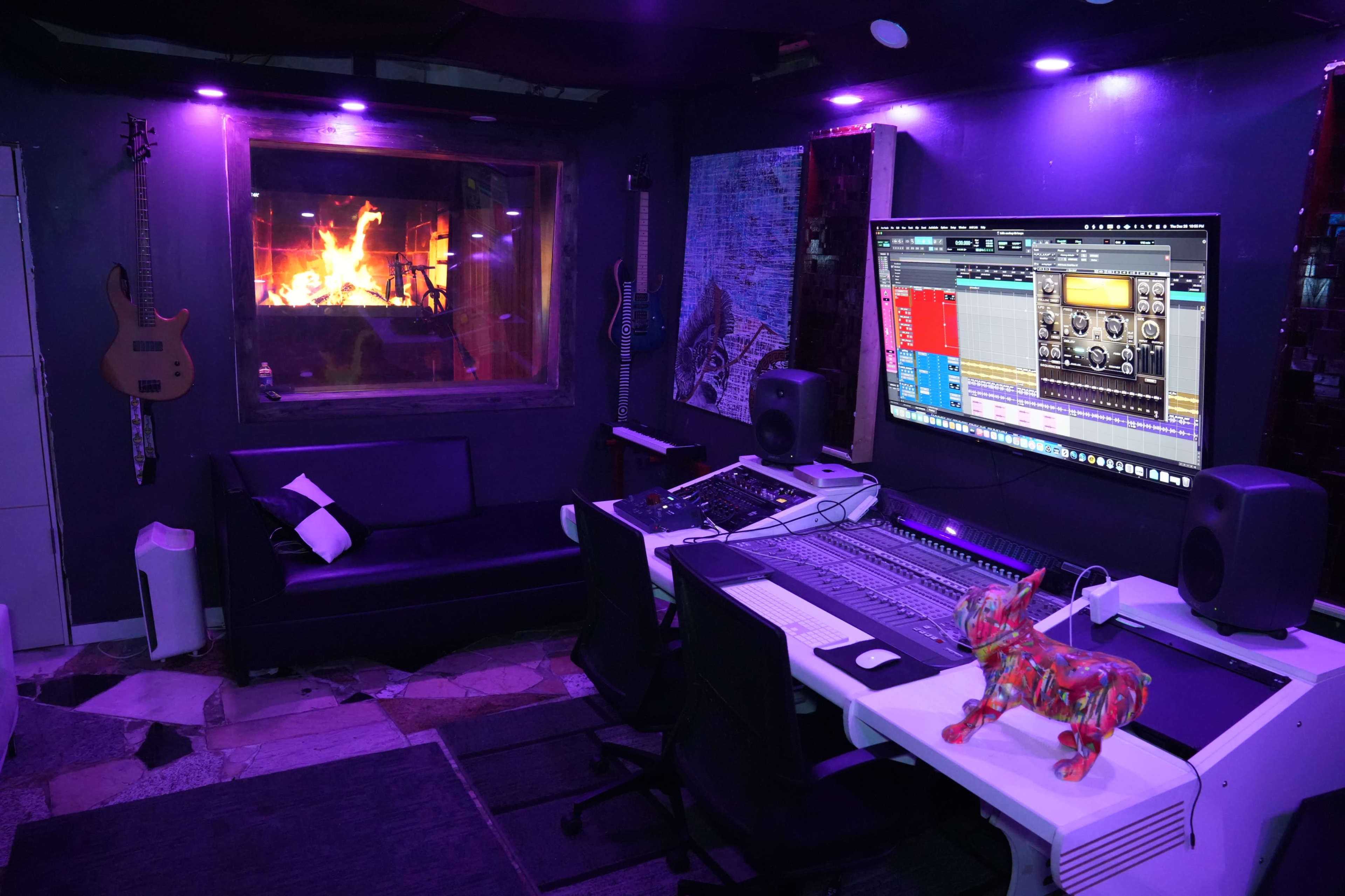 A music production studio featuring a large mixing console, monitors, a couch, and a window with a visible fire outside.