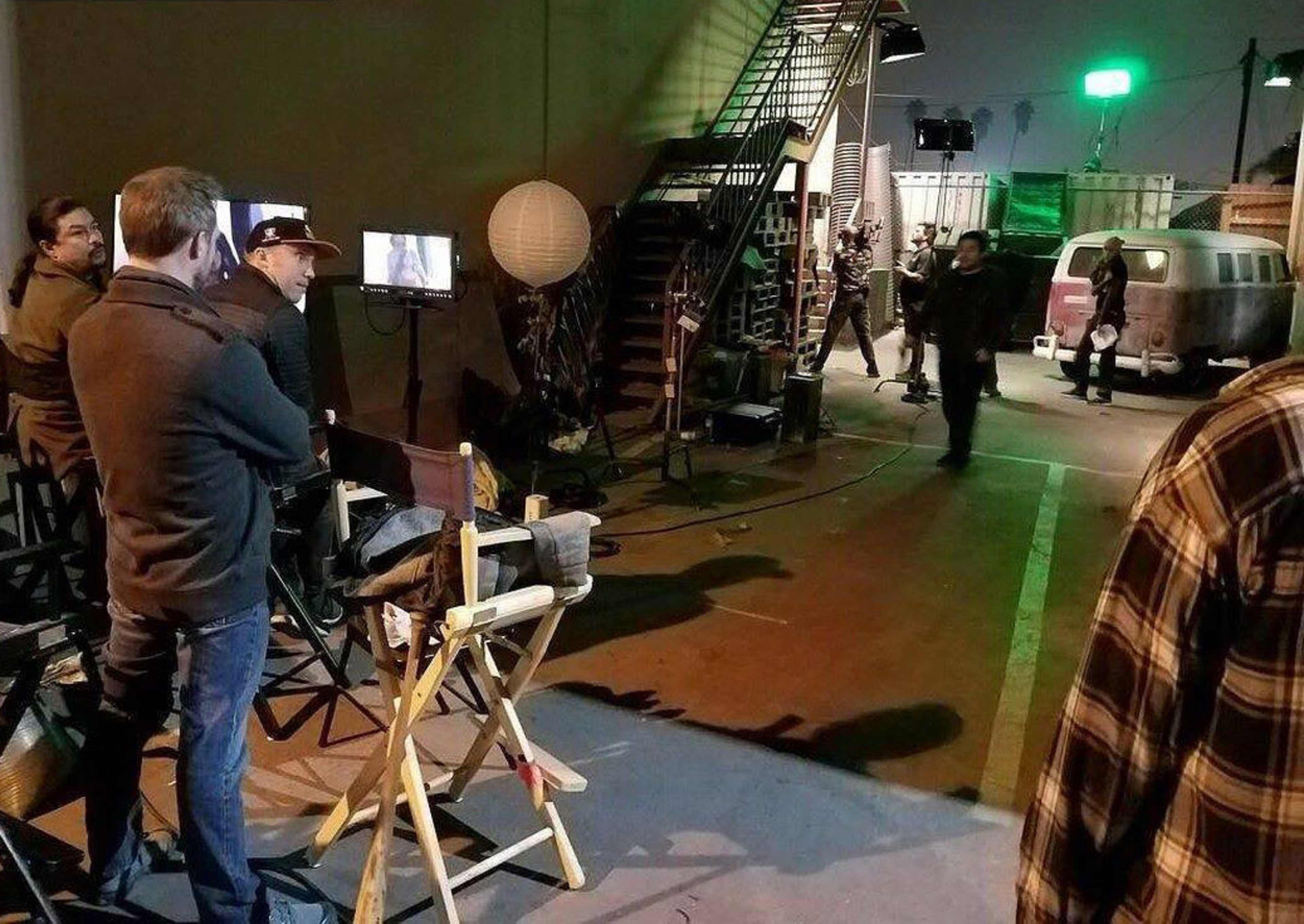 A film crew monitors a scene being shot on a set featuring a vintage van and studio equipment.