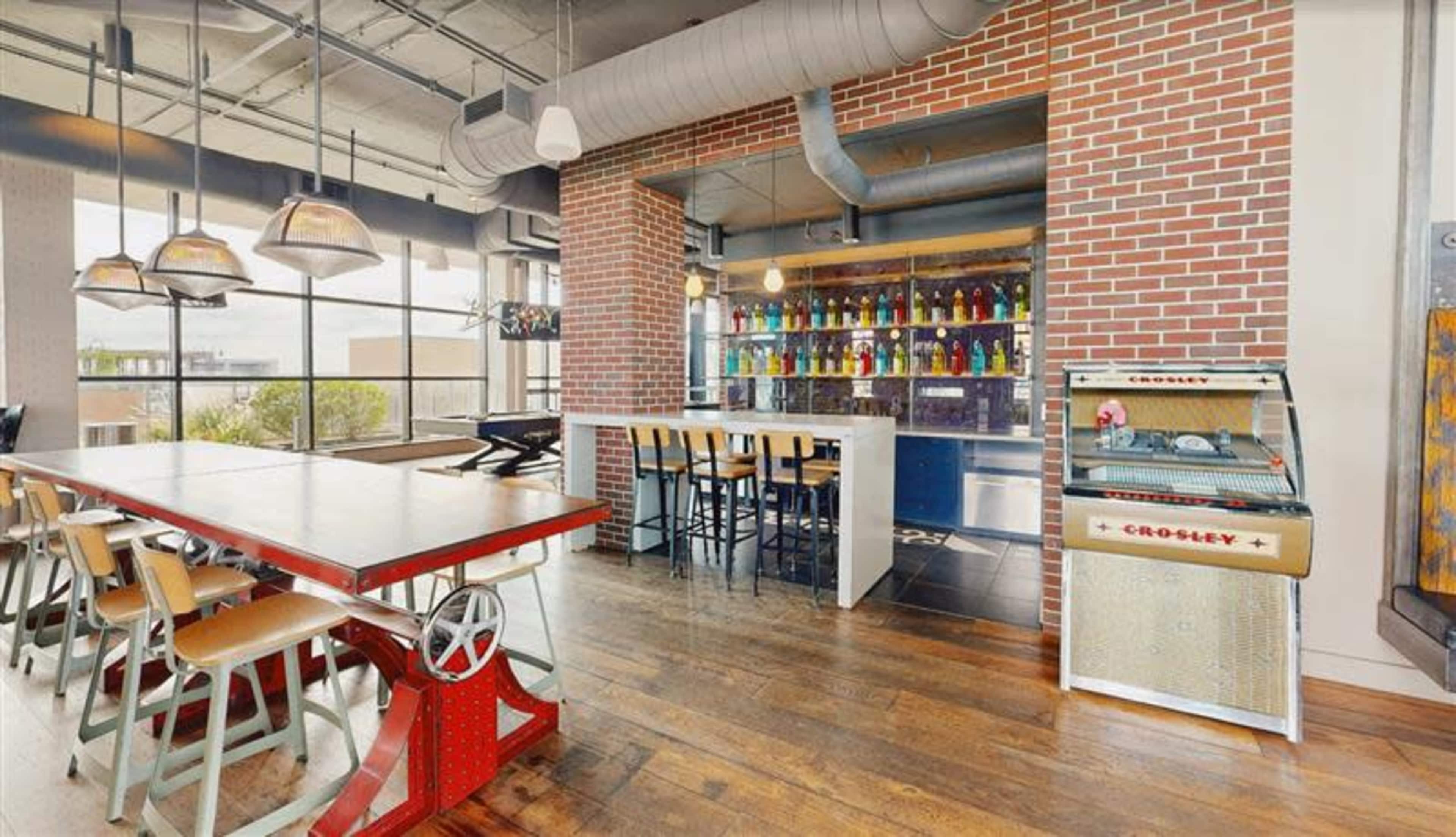 A spacious dining area features a large communal table, bar seating, and a vintage-style record player alongside a colorful display of bottles on the wall.