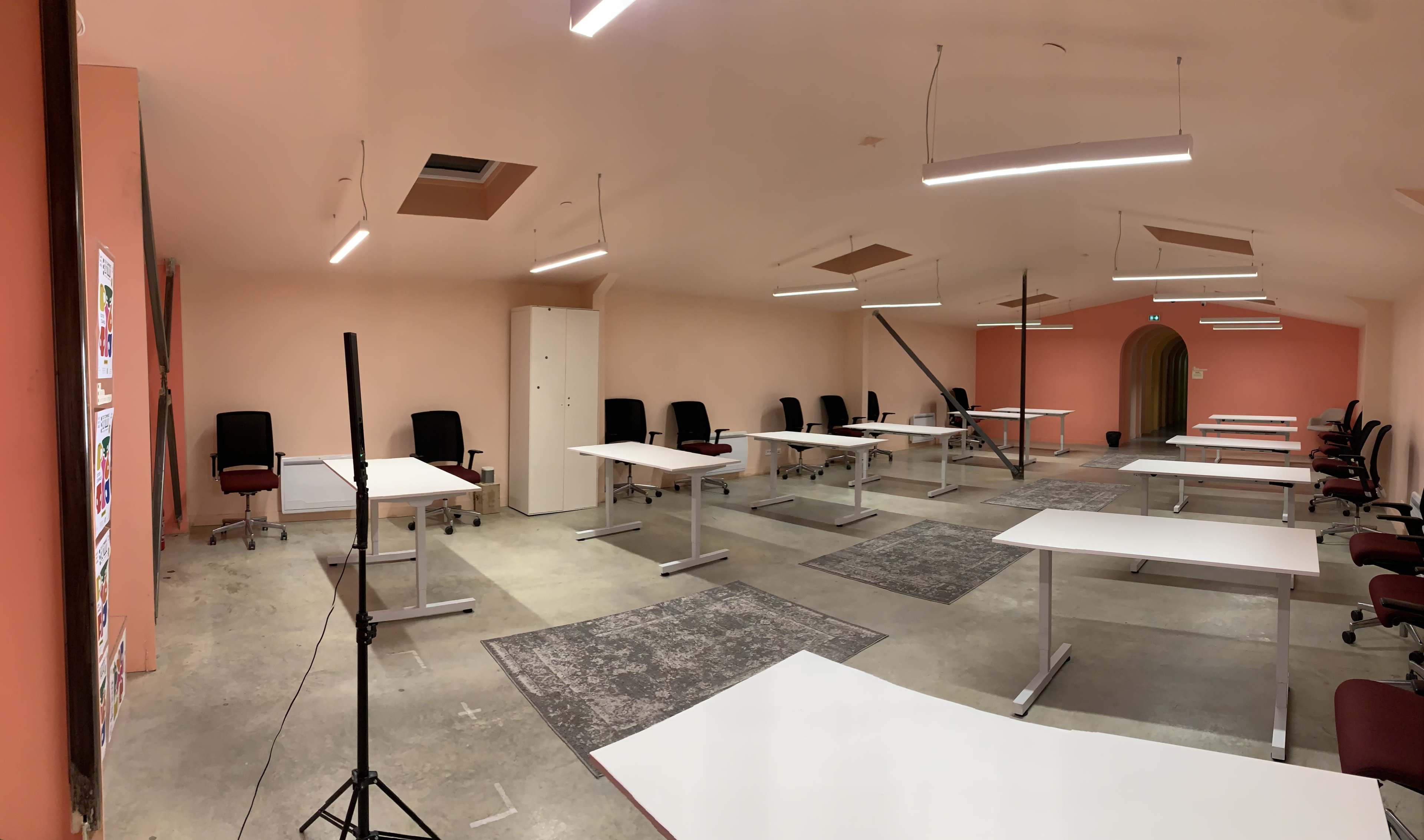 A spacious, empty office with several desks arranged in rows and chairs placed at them, all under bright overhead lighting.
