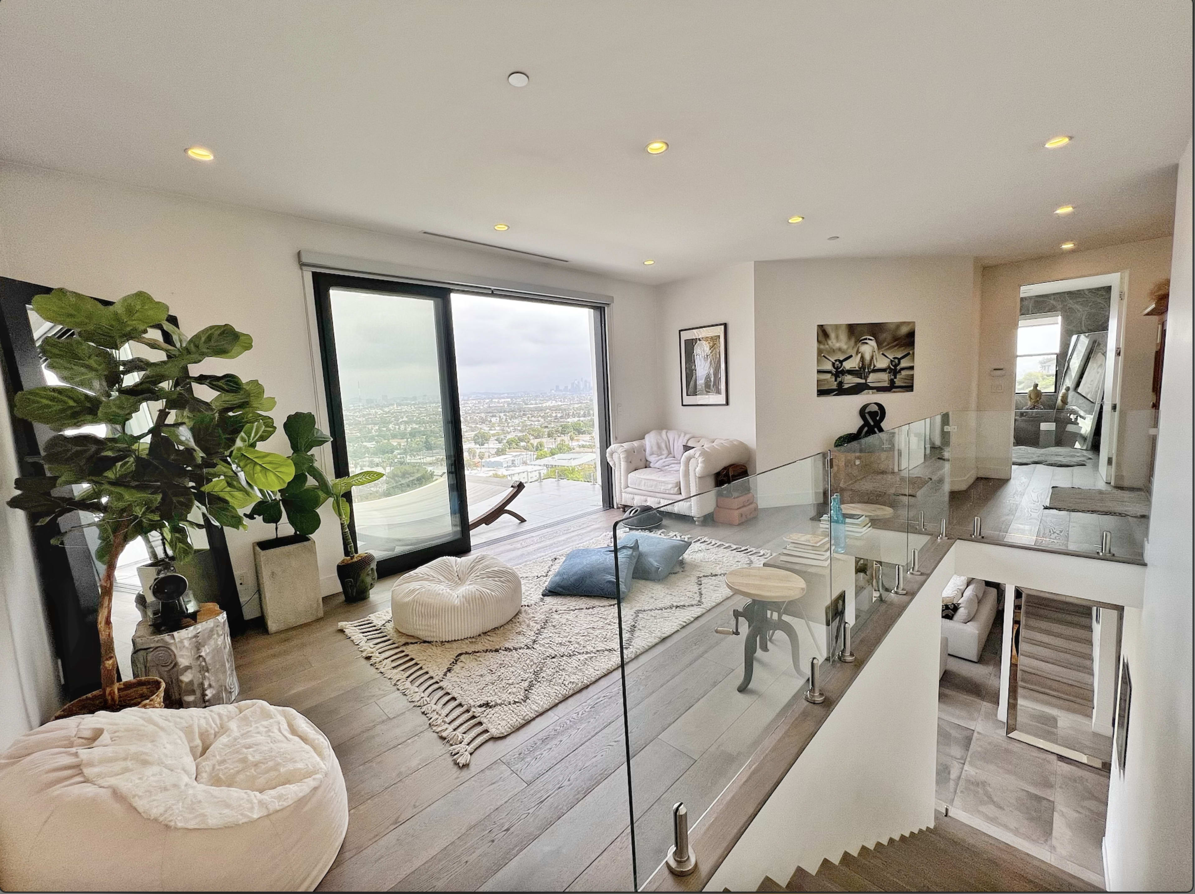 A modern living space features large windows with a view, a cozy seating area, and a staircase leading to another level.