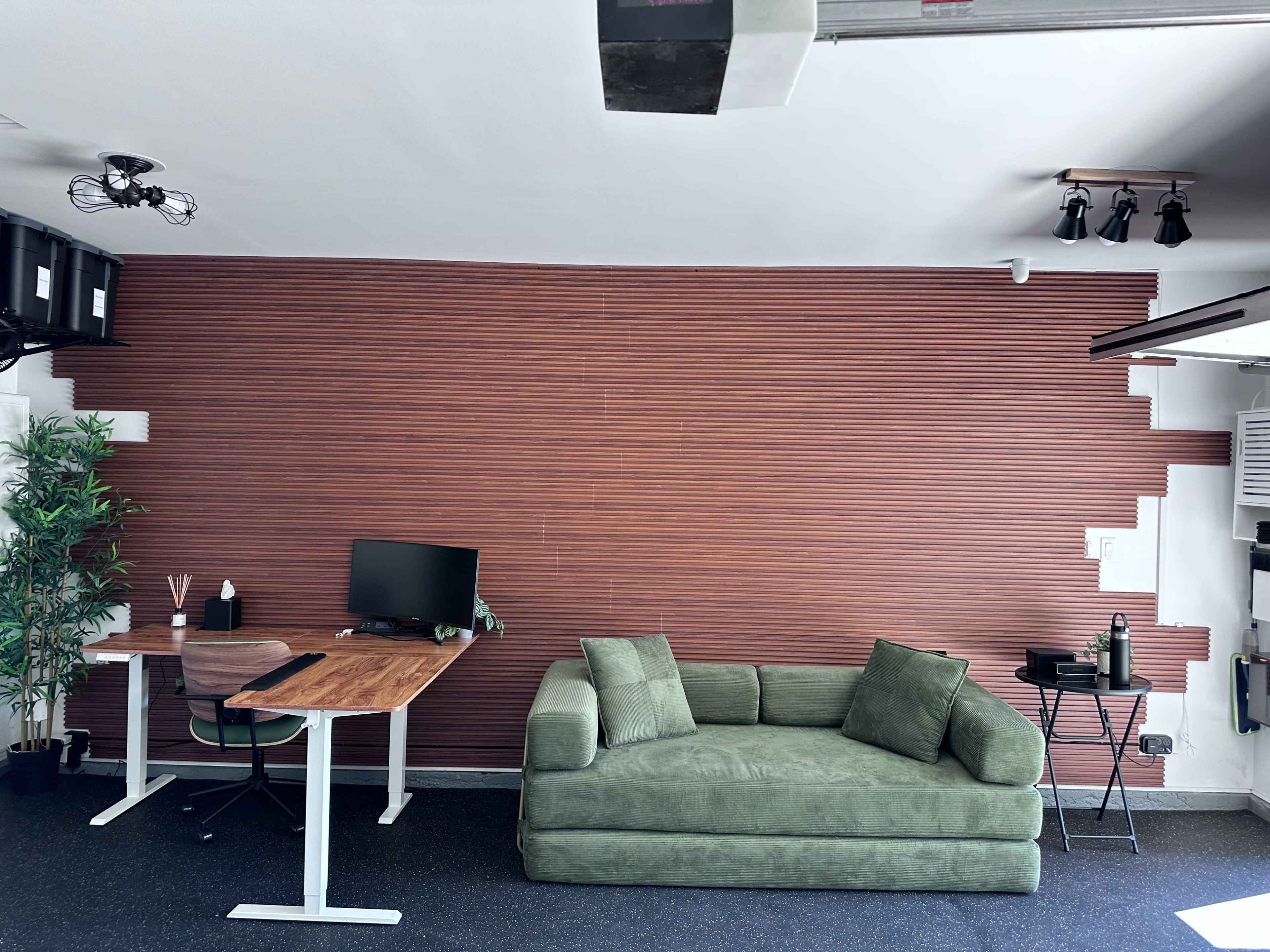 The image features a modern workspace with a green couch, a wooden desk with a computer, and a textured brown wall.