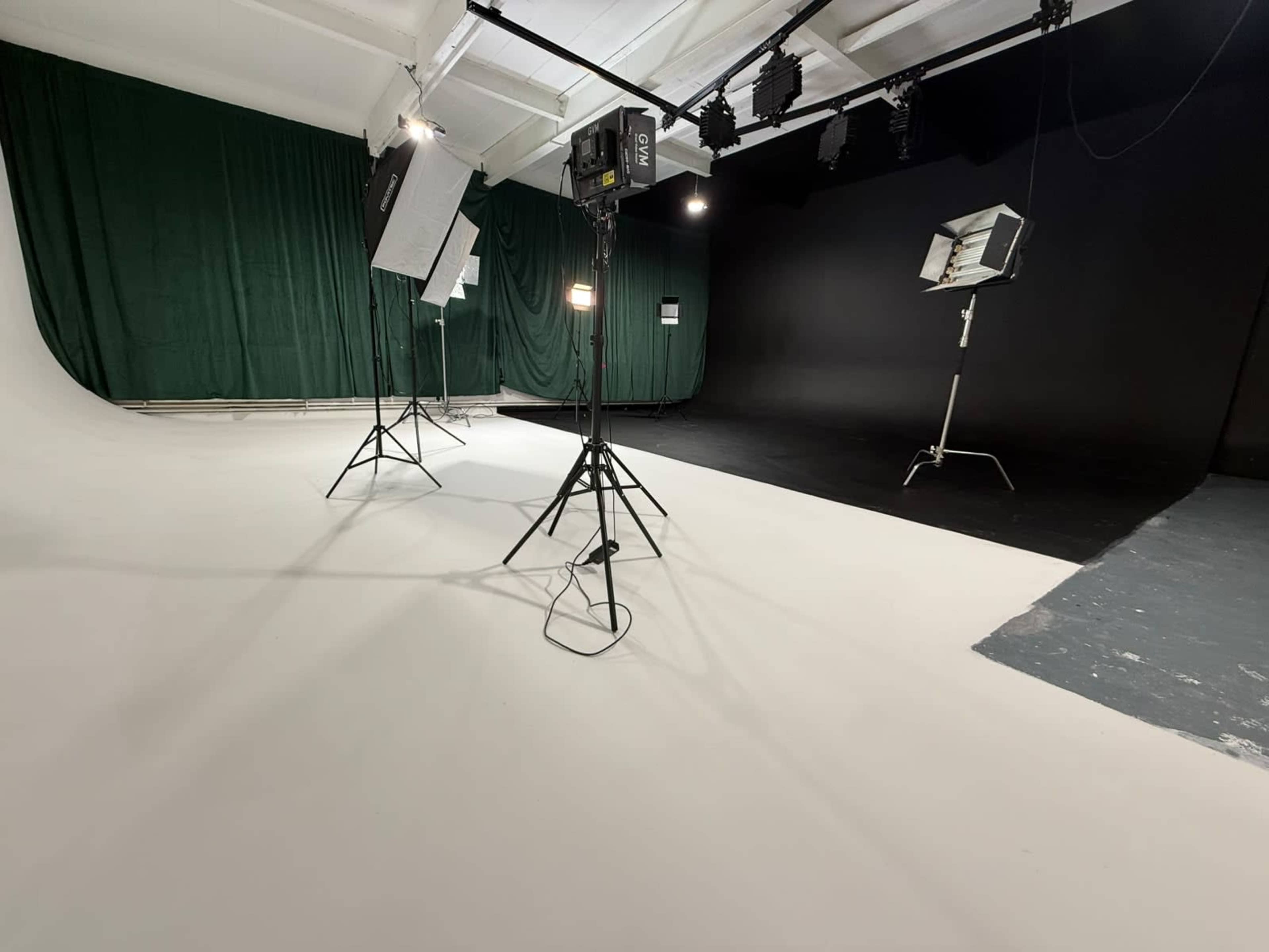 The image shows a photography studio with a white floor, green backdrop, and various lighting equipment set up on tripods.