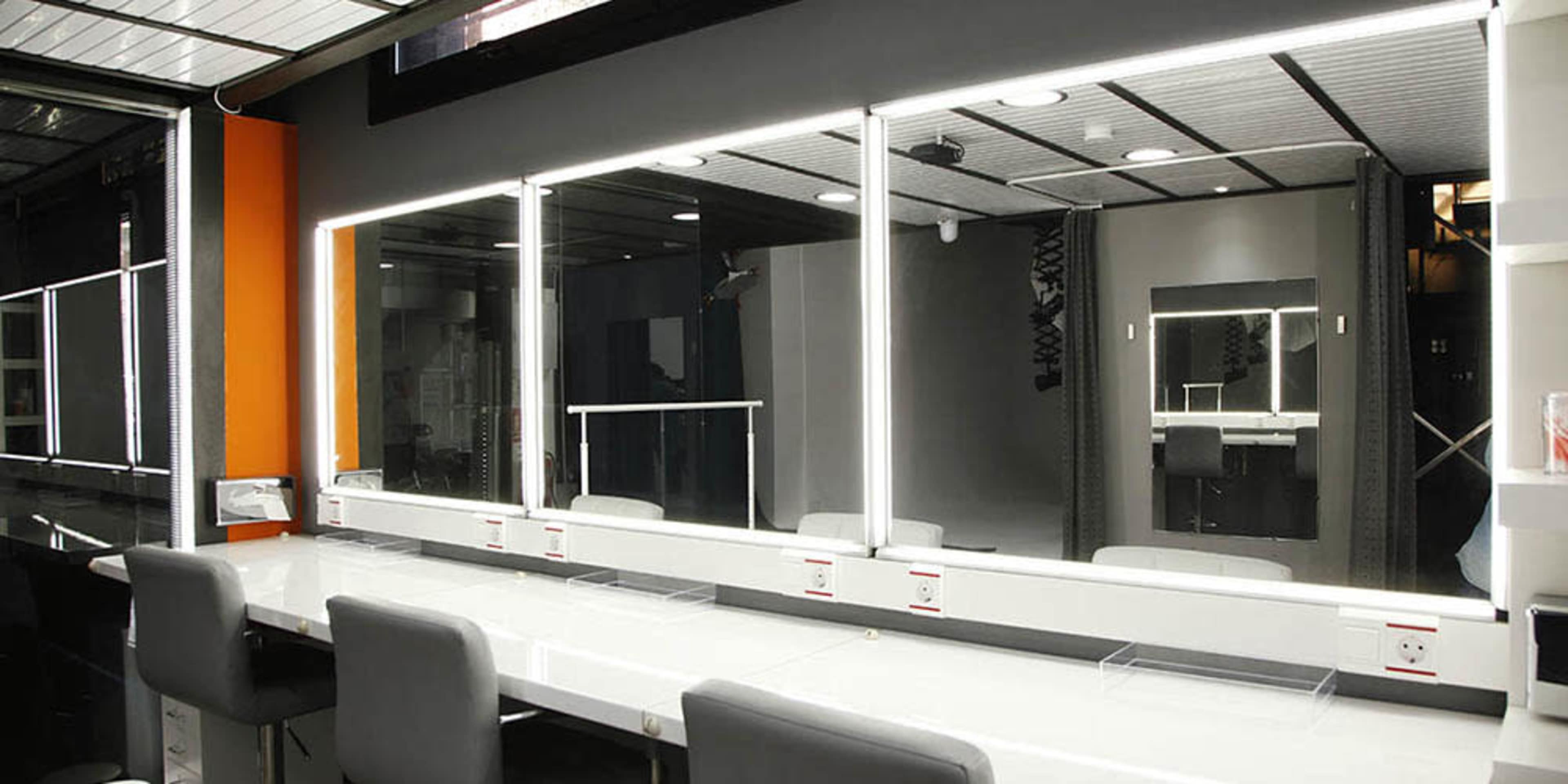 A modern dressing room with illuminated mirrors and several high-backed chairs arranged in front of a long countertop.