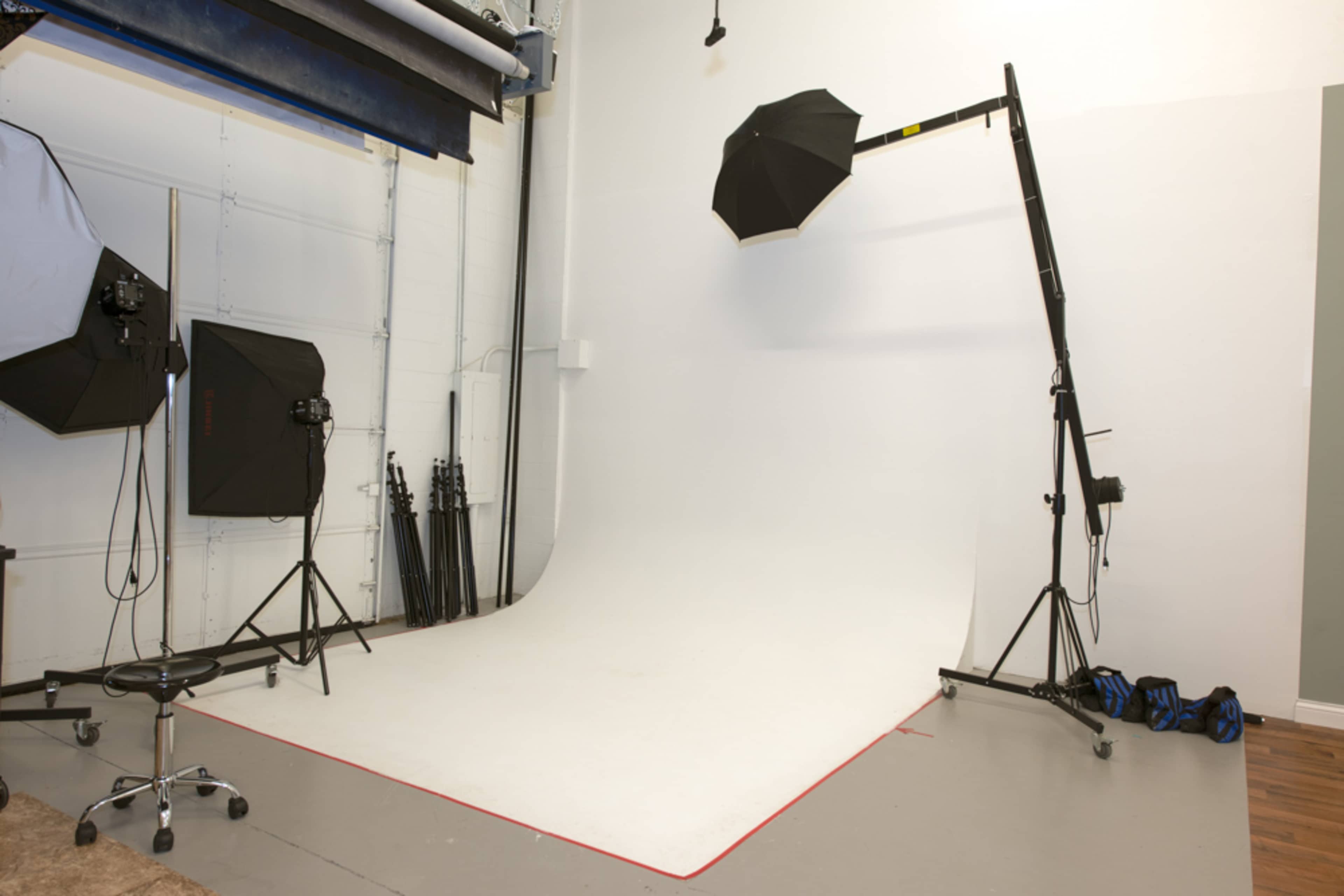 A photography studio features a white curved backdrop with lighting equipment and tripods arranged around it.