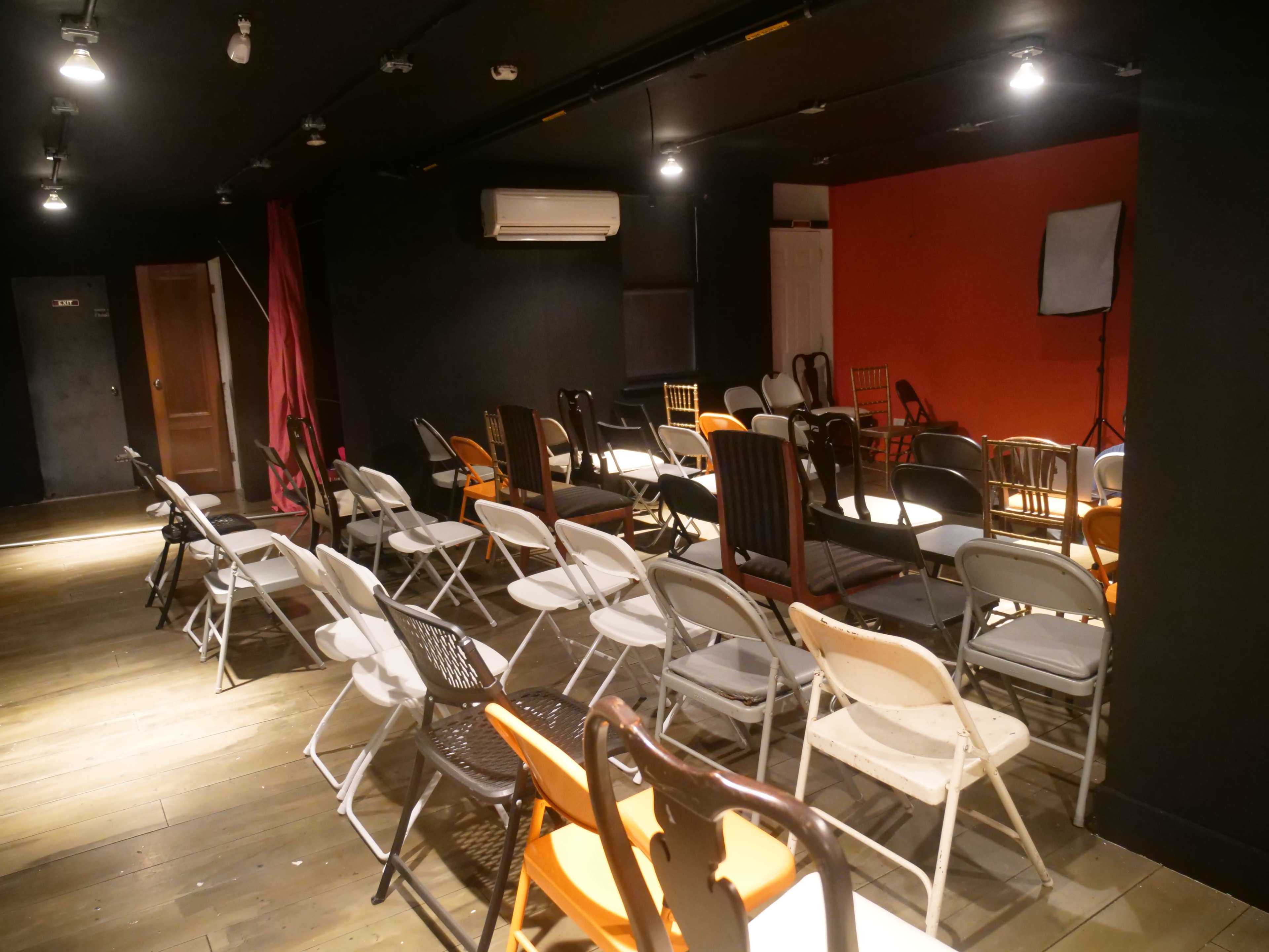 A room with a combination of wooden and metal chairs arranged around several small tables, illuminated by overhead lights.