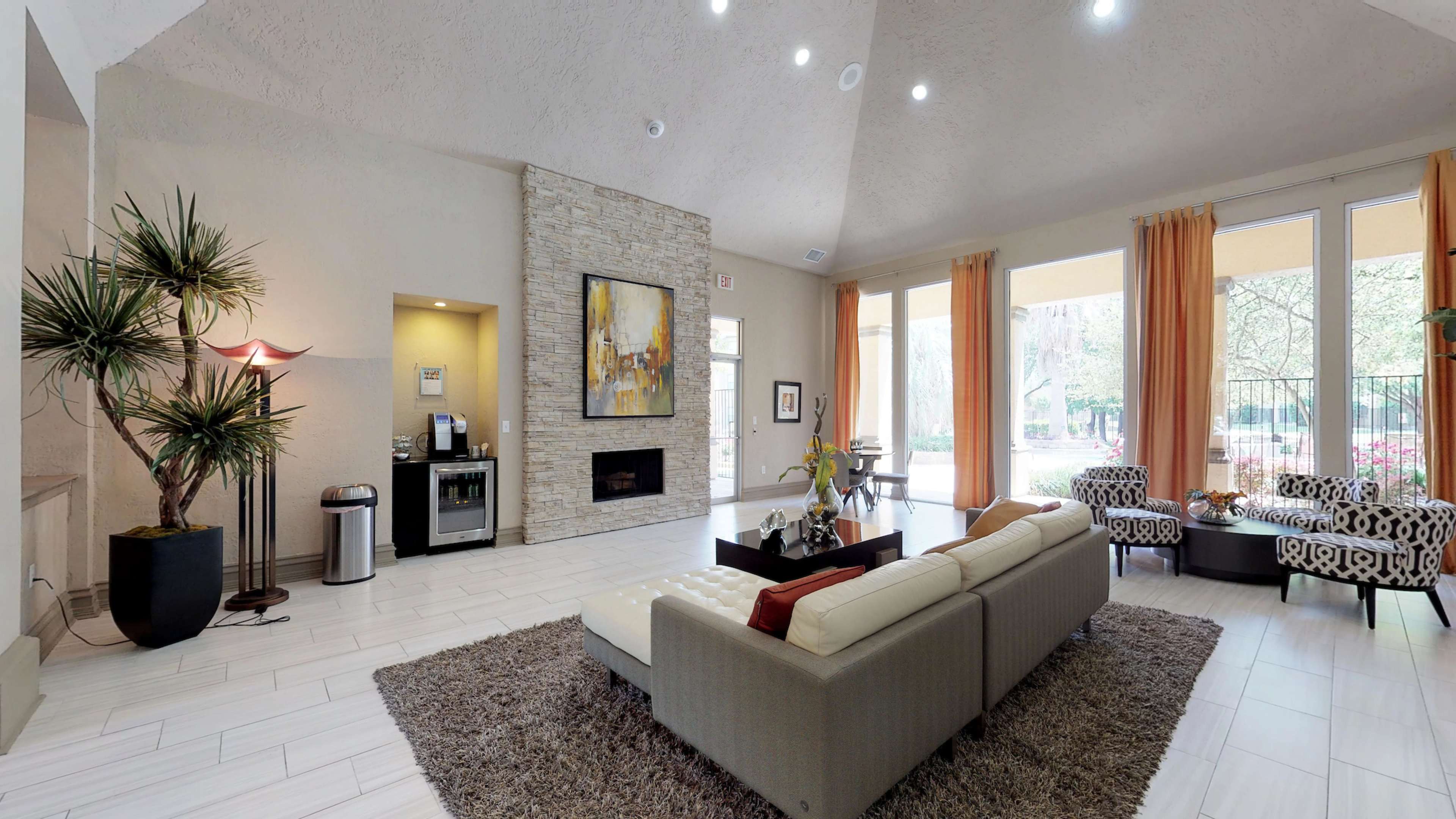 A modern living room with a stone fireplace, a beige sofa, a coffee table, and large windows draped with orange curtains.