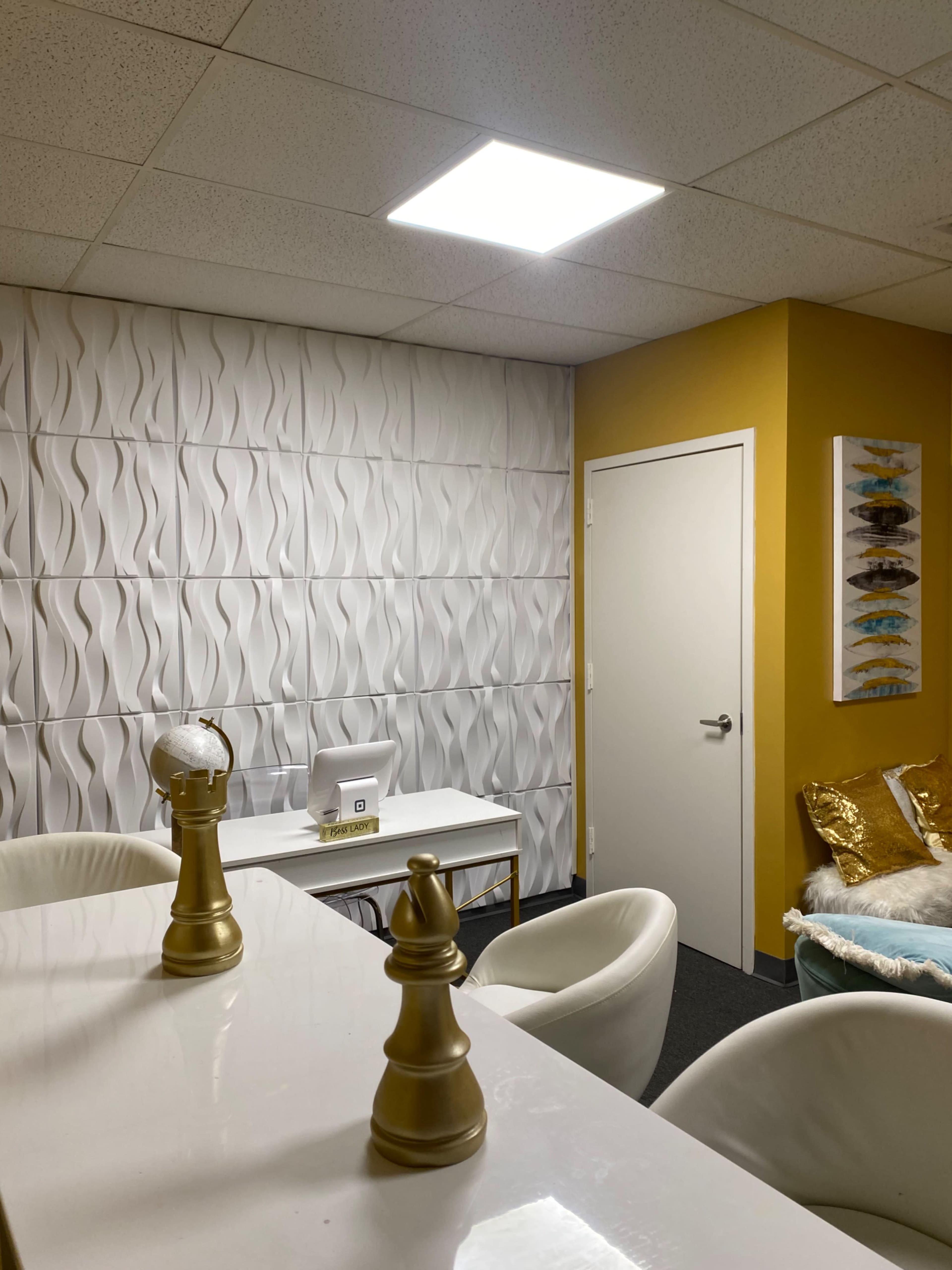 A modern office space with a textured white wall, a golden-yellow accent wall, a white table, and decorative items including chess pieces and artwork.