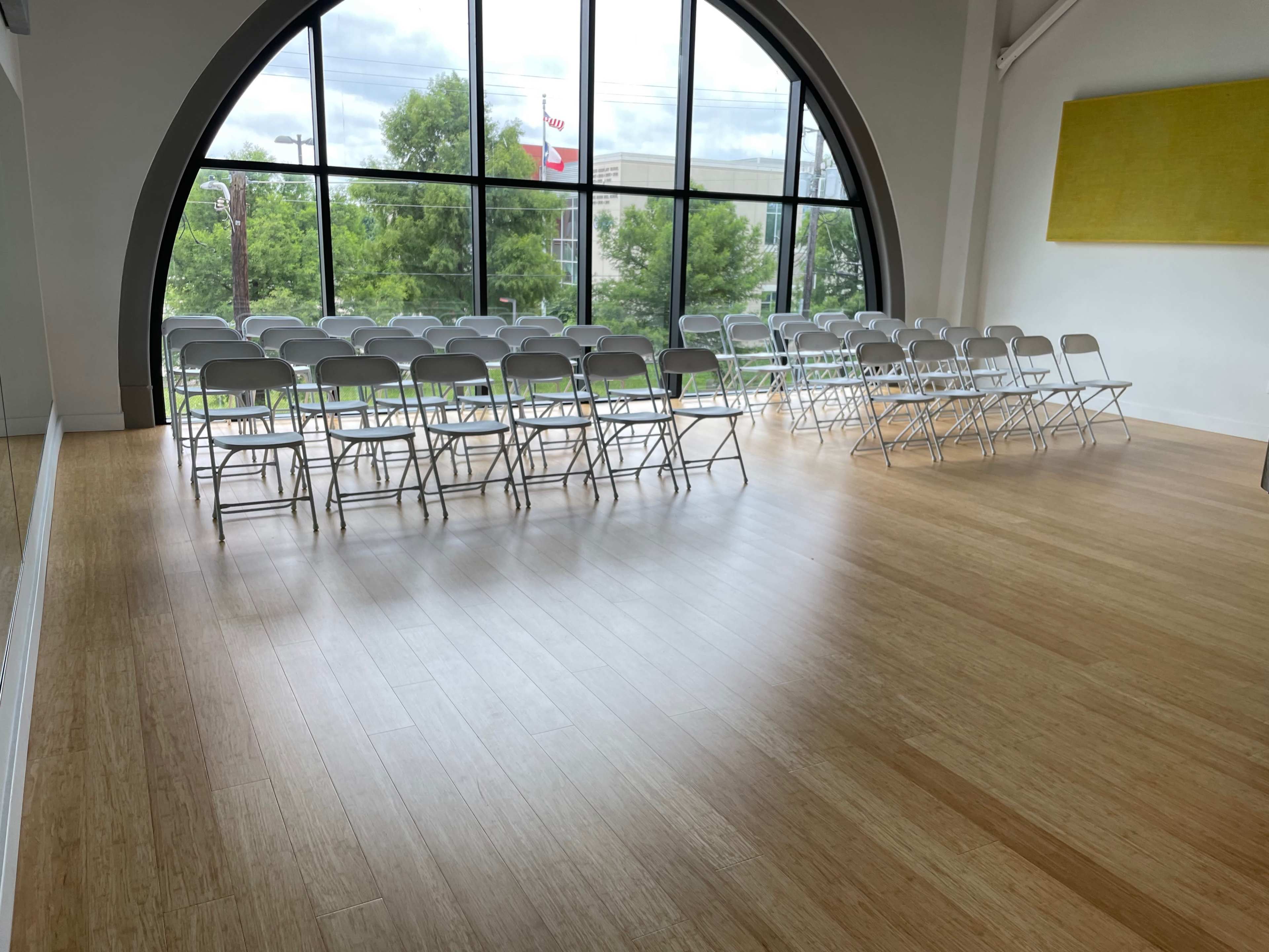 The image shows a spacious room with rows of white folding chairs arranged facing a large arched window.