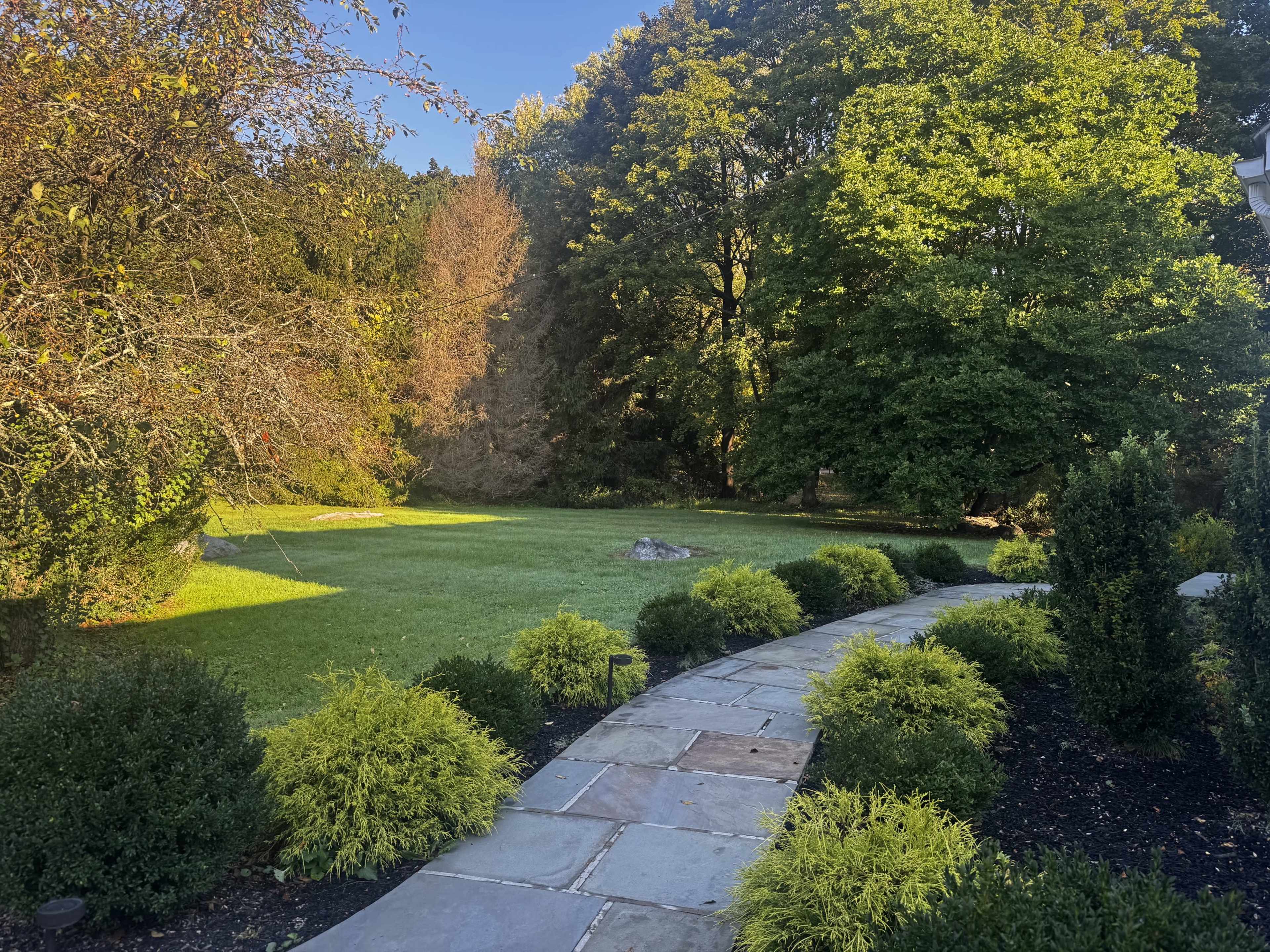 A stone pathway leads through a manicured lawn surrounded by lush greenery and trees.