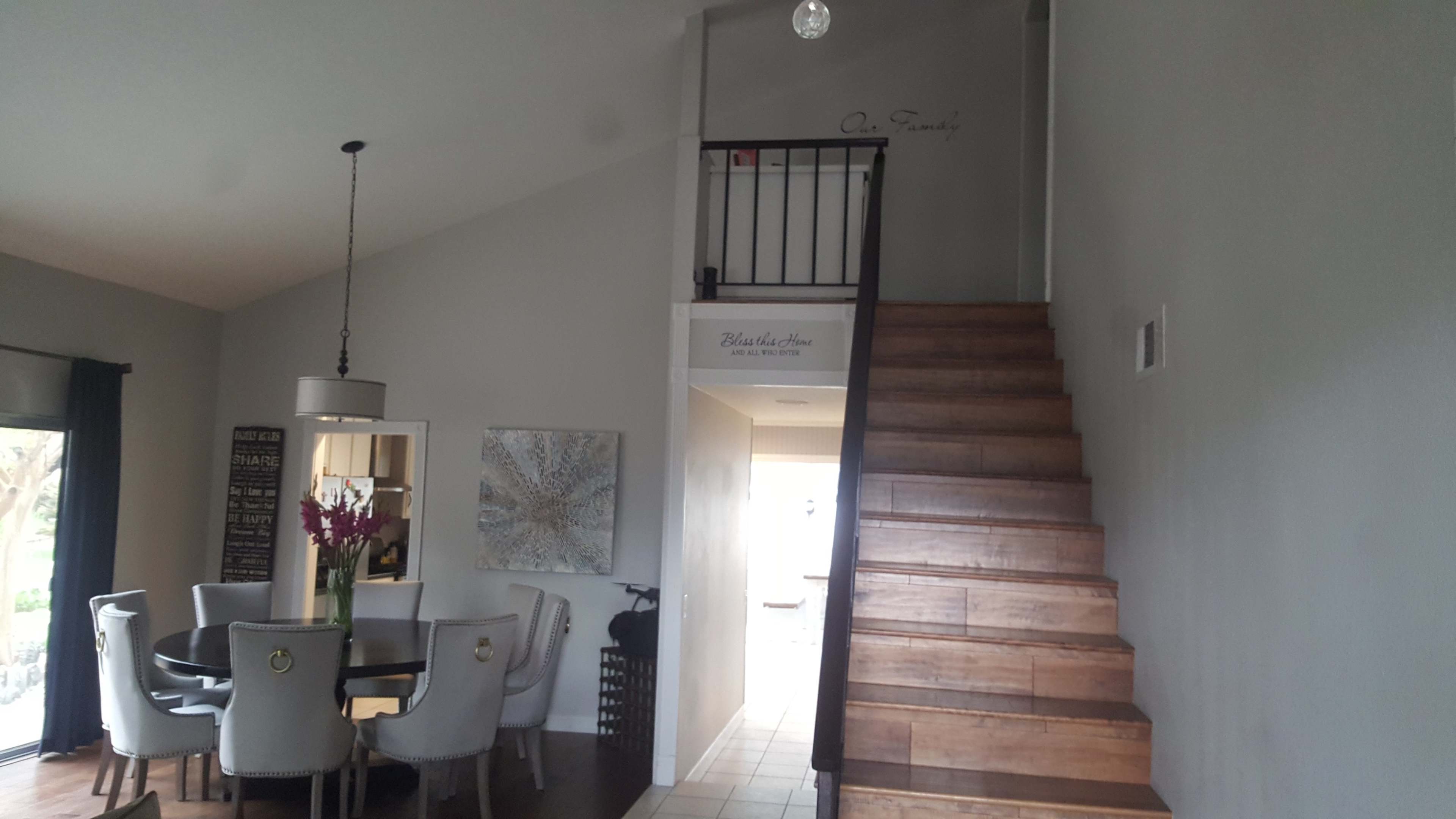 A modern interior with a staircase leading to an upper level, a dining area with a circular table and chairs, and a light fixture above.