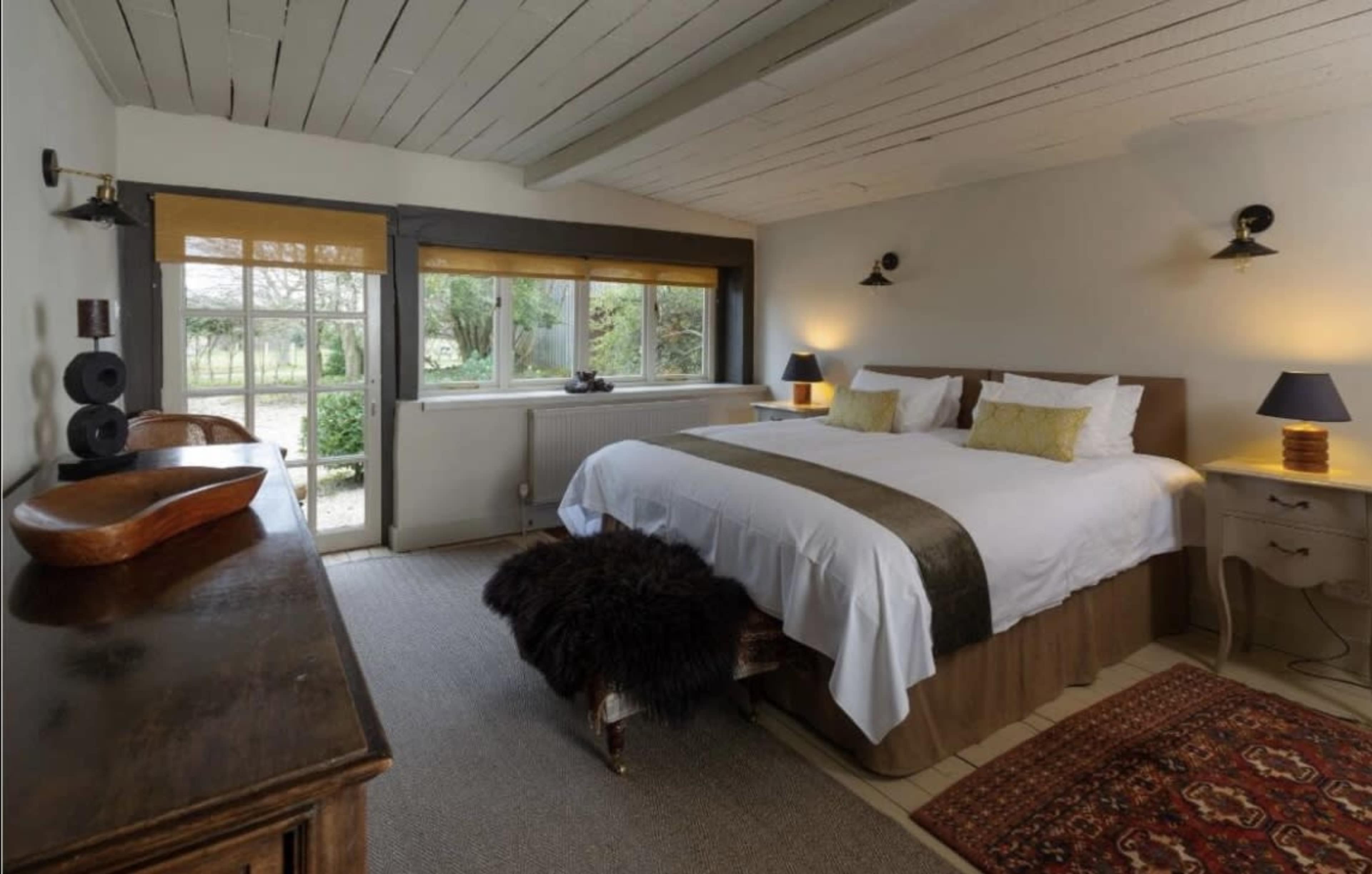 A spacious bedroom with a double bed, wooden furniture, and large windows overlooking a garden.