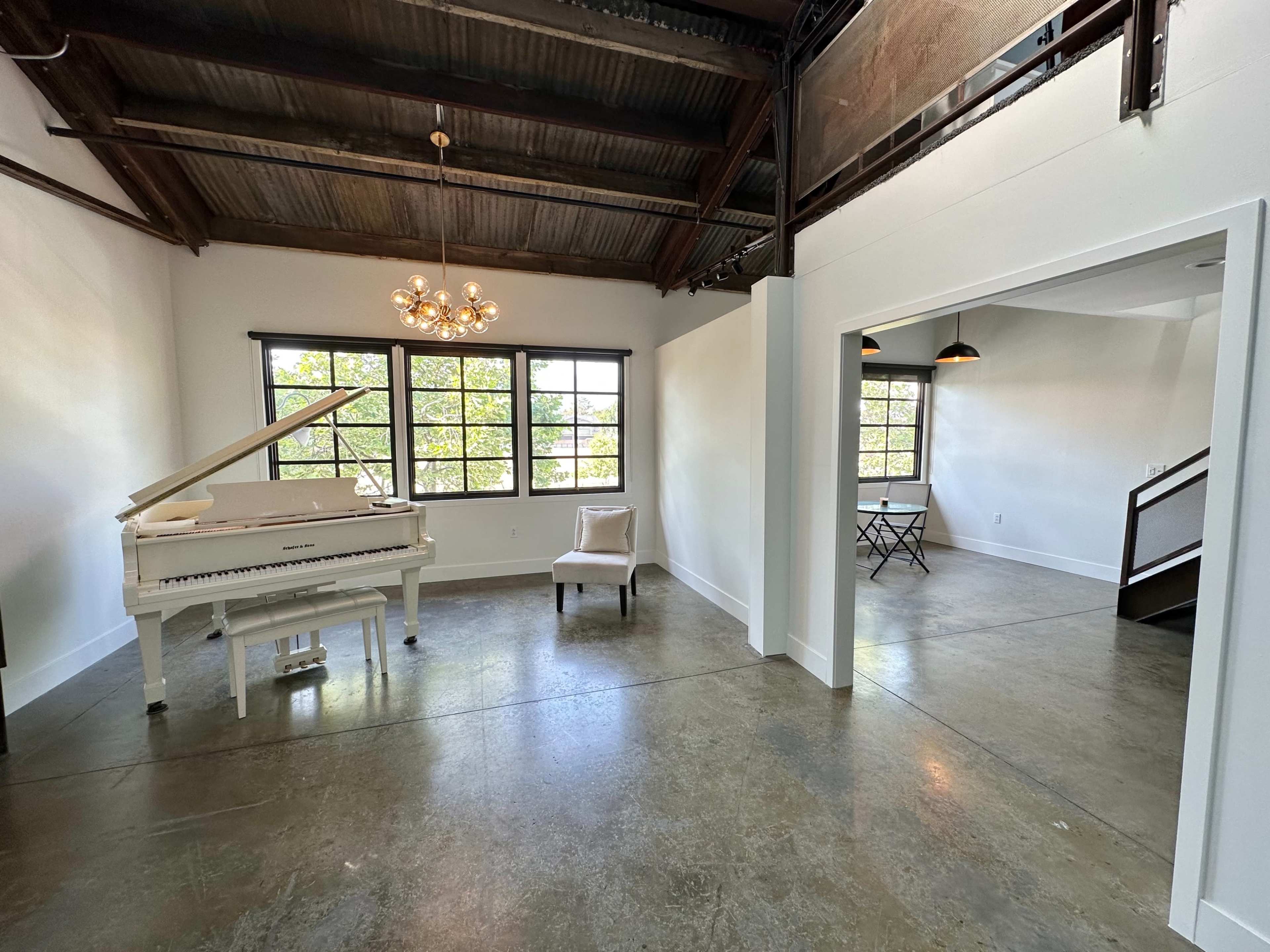 A bright, open living space featuring a white piano, a single chair, and large windows allowing natural light to enter.