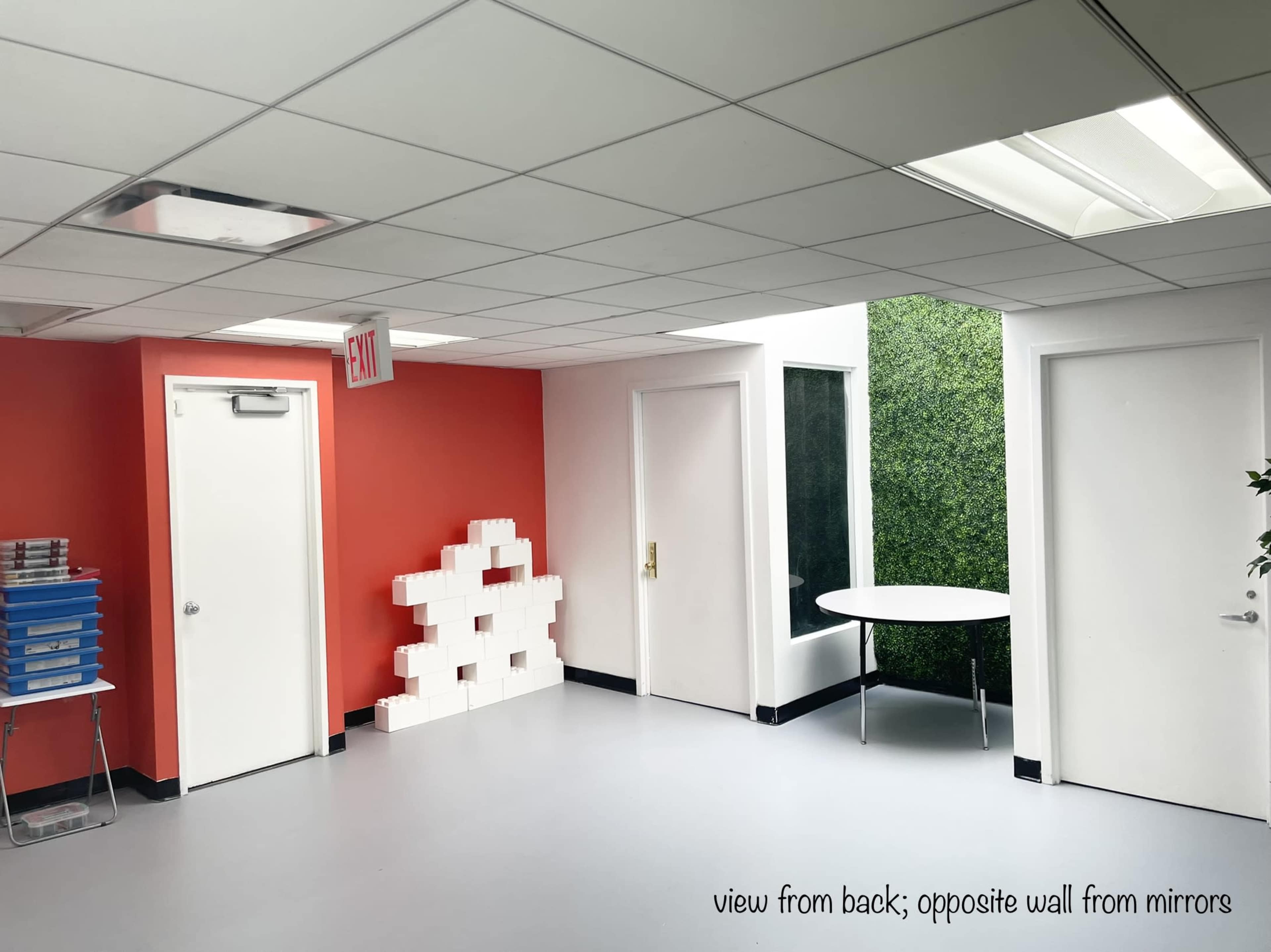 A bright, modern room with red and white walls, featuring two doors, a green wall, and a circular table in the corner.