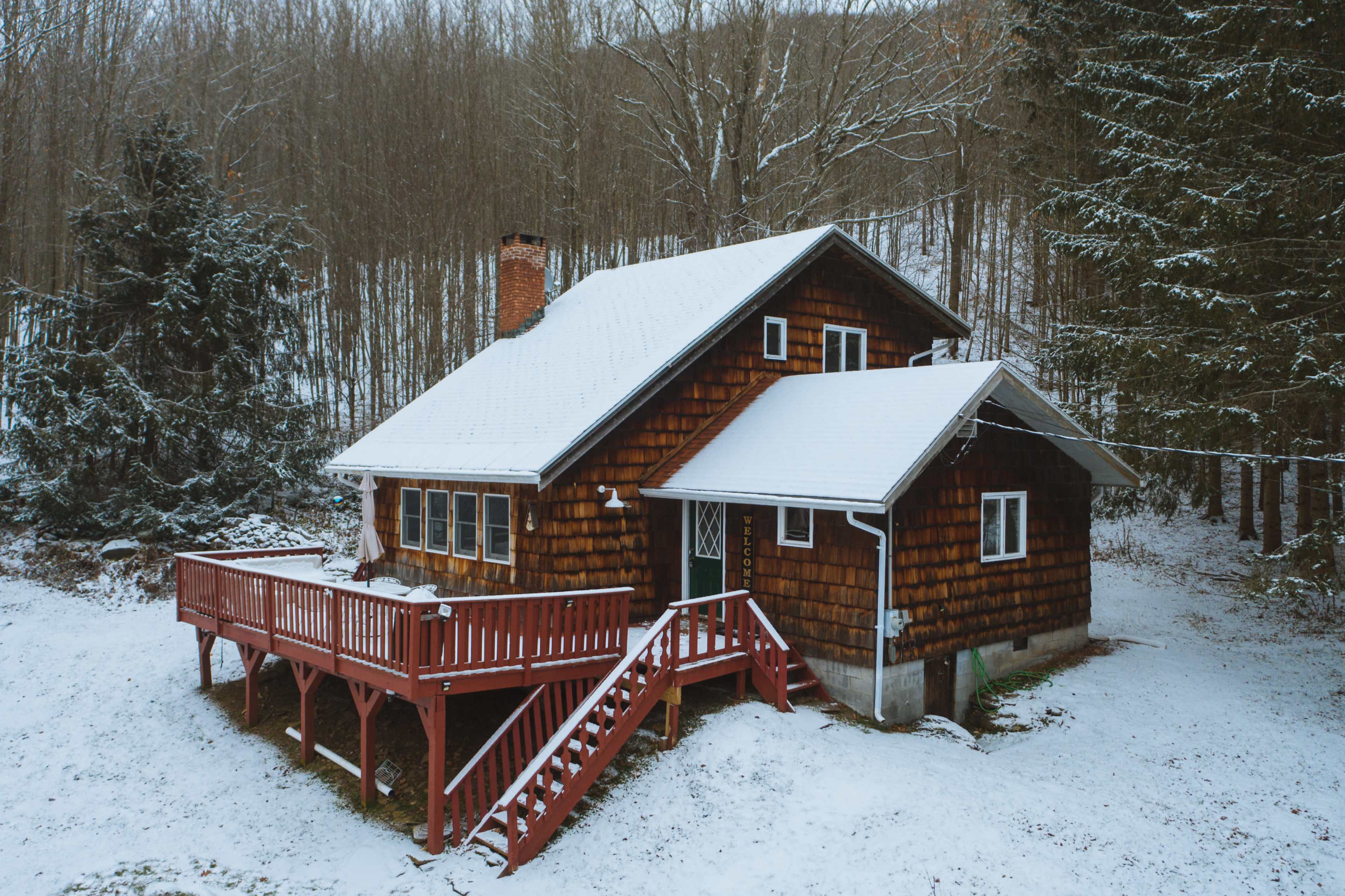 A wooden cabin with a red deck sits surrounded by snow-covered ground and forested land.