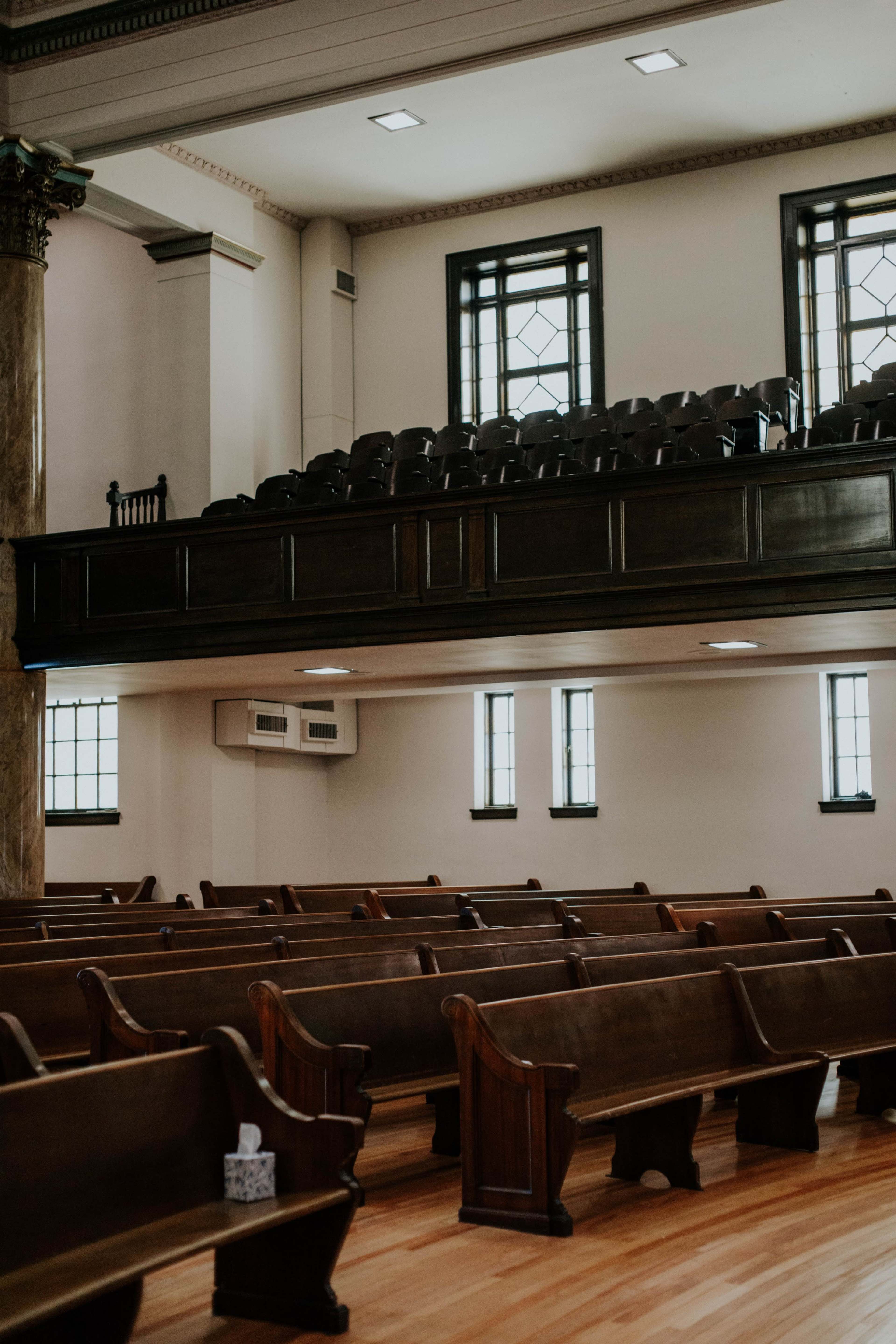 The image shows an interior of a spacious church with wooden pews arranged in rows and a balcony with additional seating above.