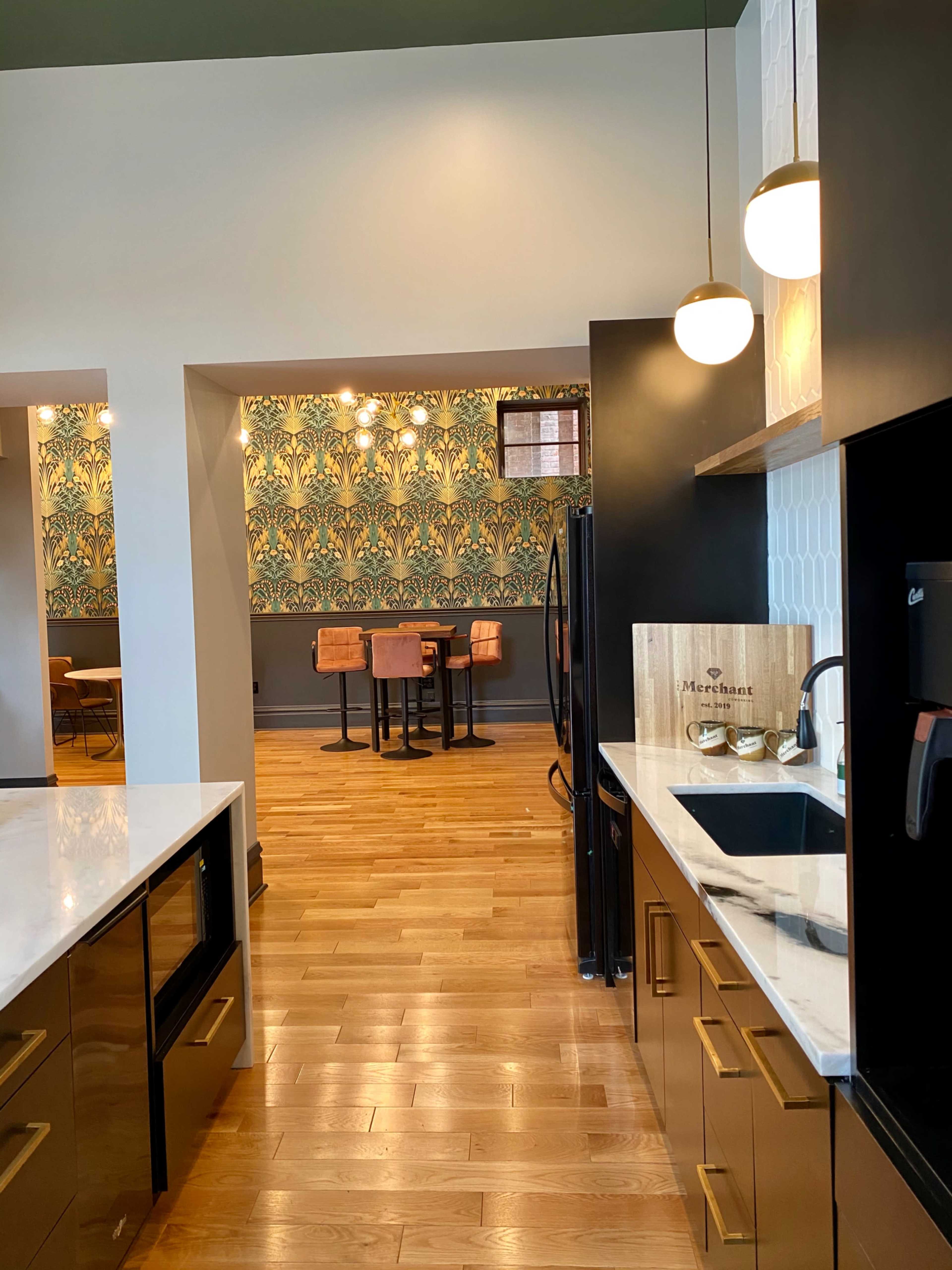 The image shows a modern kitchen with black cabinets and a marble countertop, leading to a dining area highlighted by patterned wallpaper and a wooden floor.
