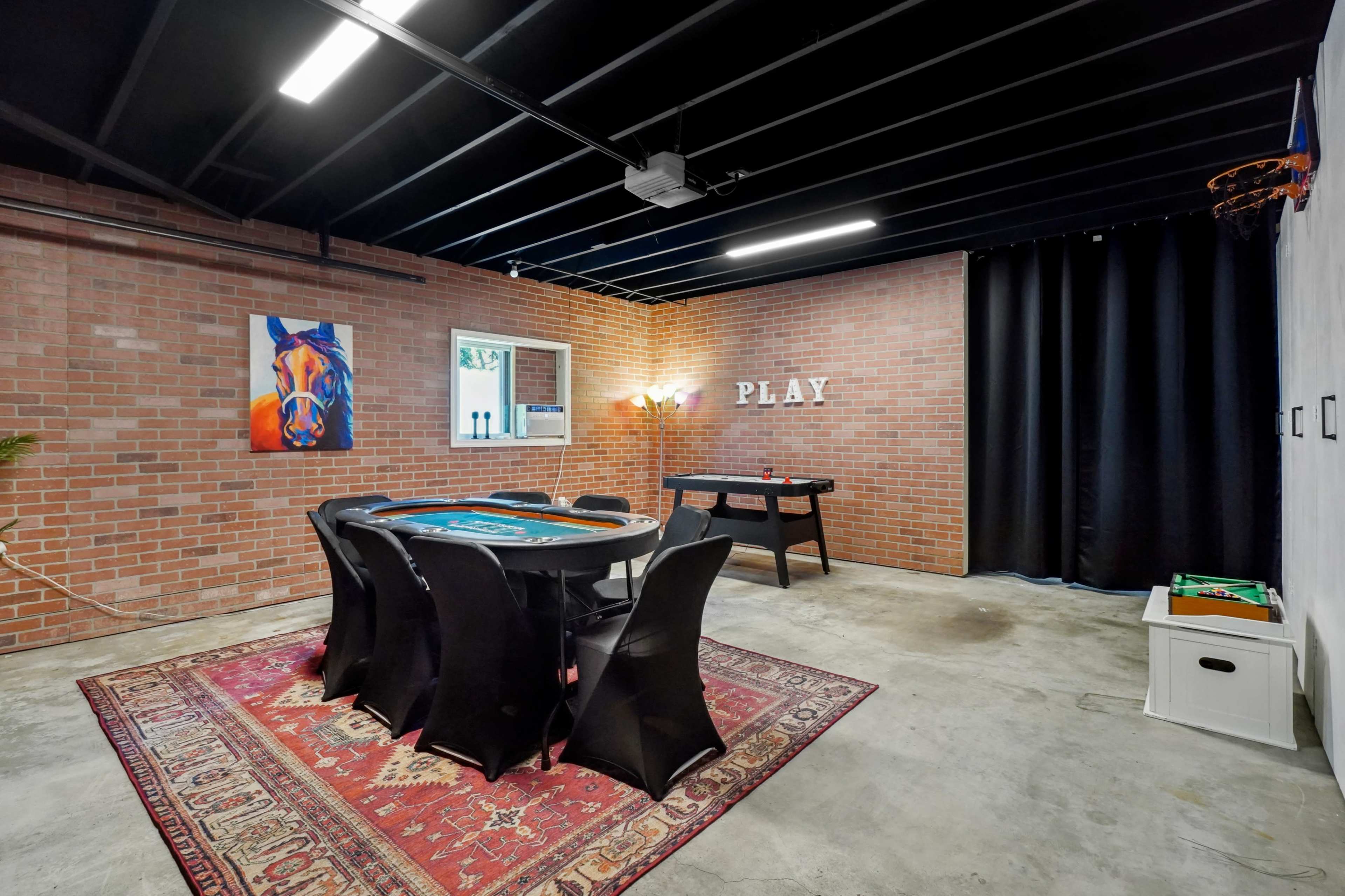 The image shows a game room featuring a poker table, a dartboard, and brick walls, with a rug on the floor and a "PLAY" sign on the wall.